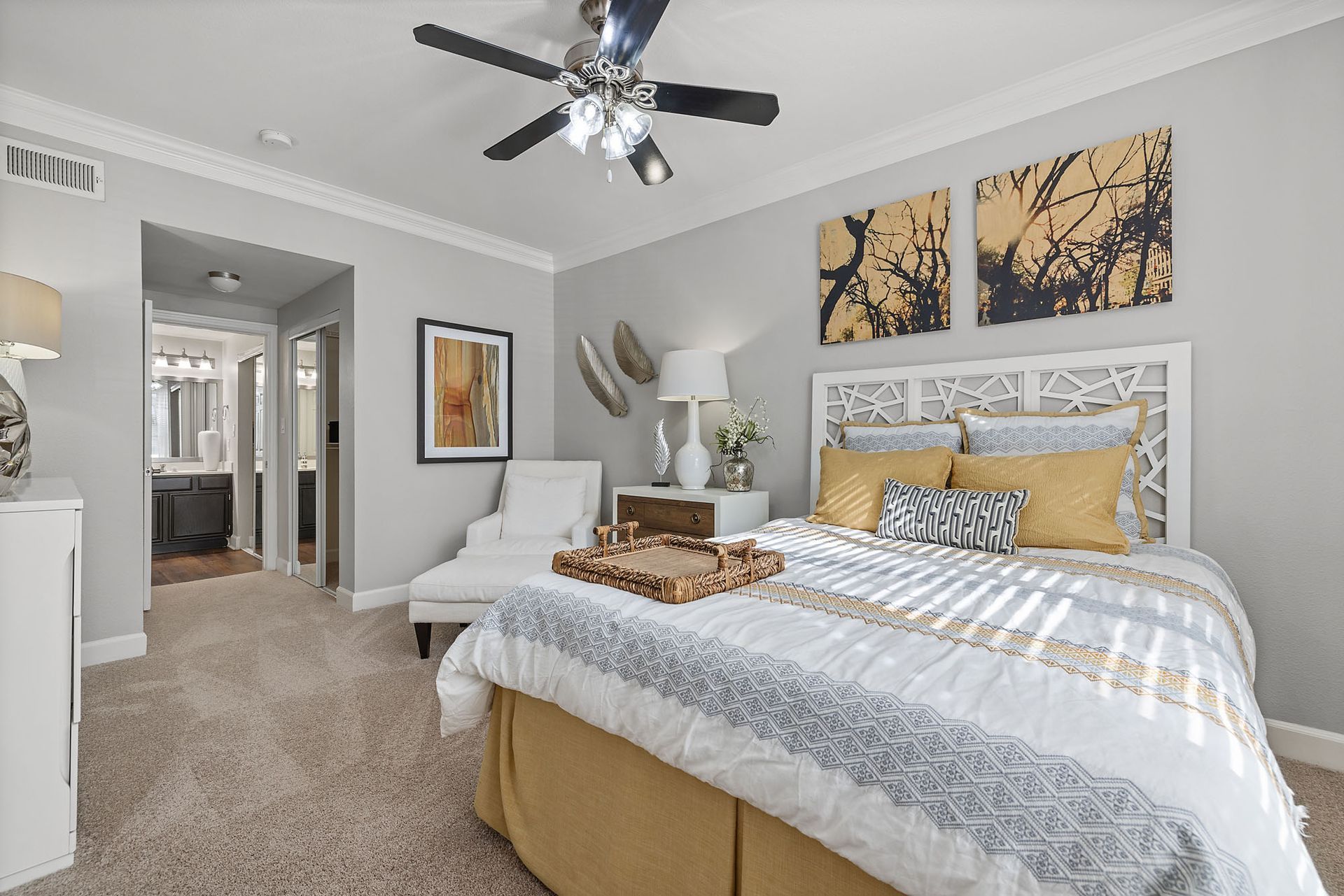 Bright bedroom with white bed, beige carpet, ceiling fan, and wall art in a neatly styled interior at Marquis at Great Hills in Austin, TX.