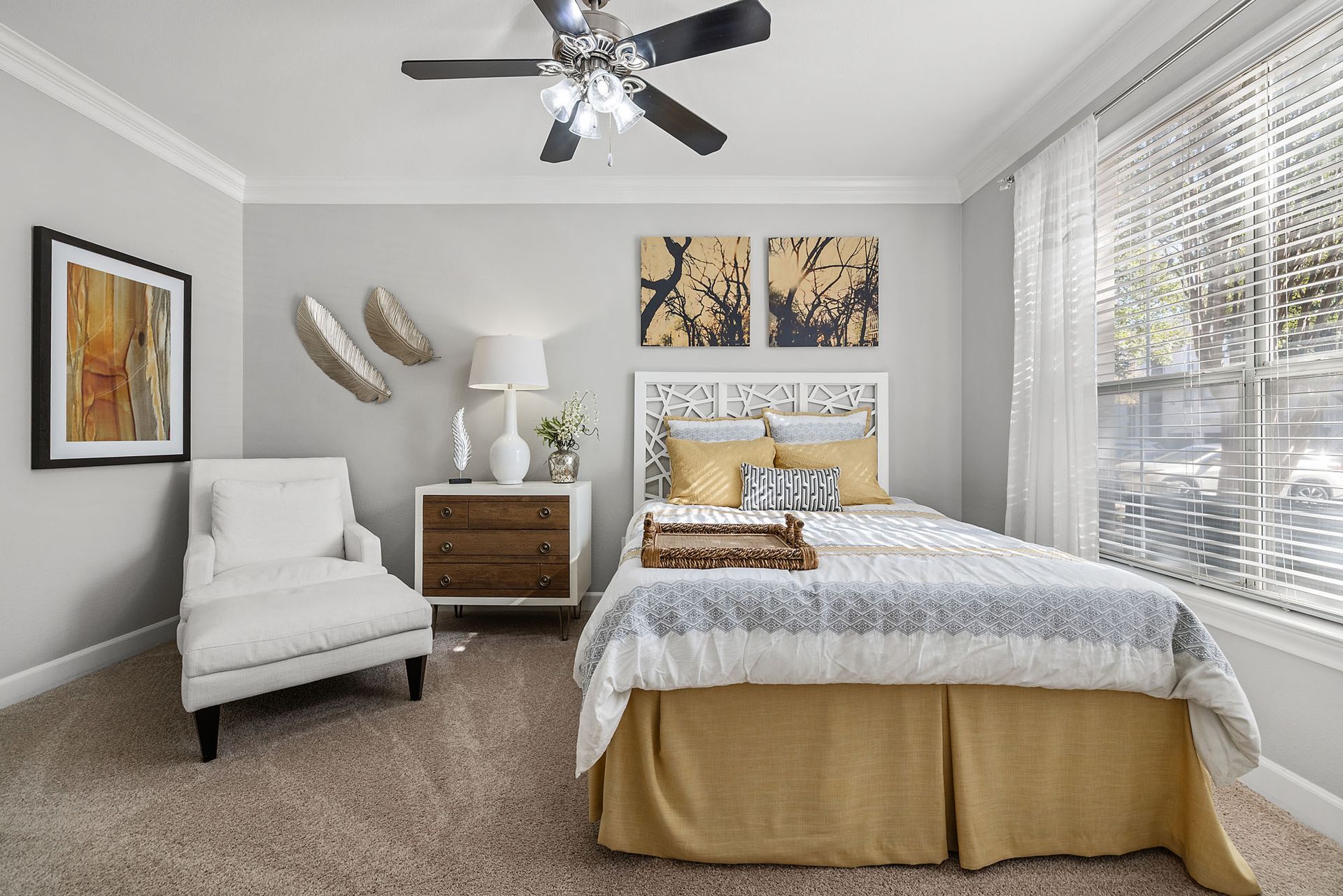 Bright bedroom with a bed, armchair, nightstand, wall art, and large window blinds at Marquis at Great Hills in Austin, TX.