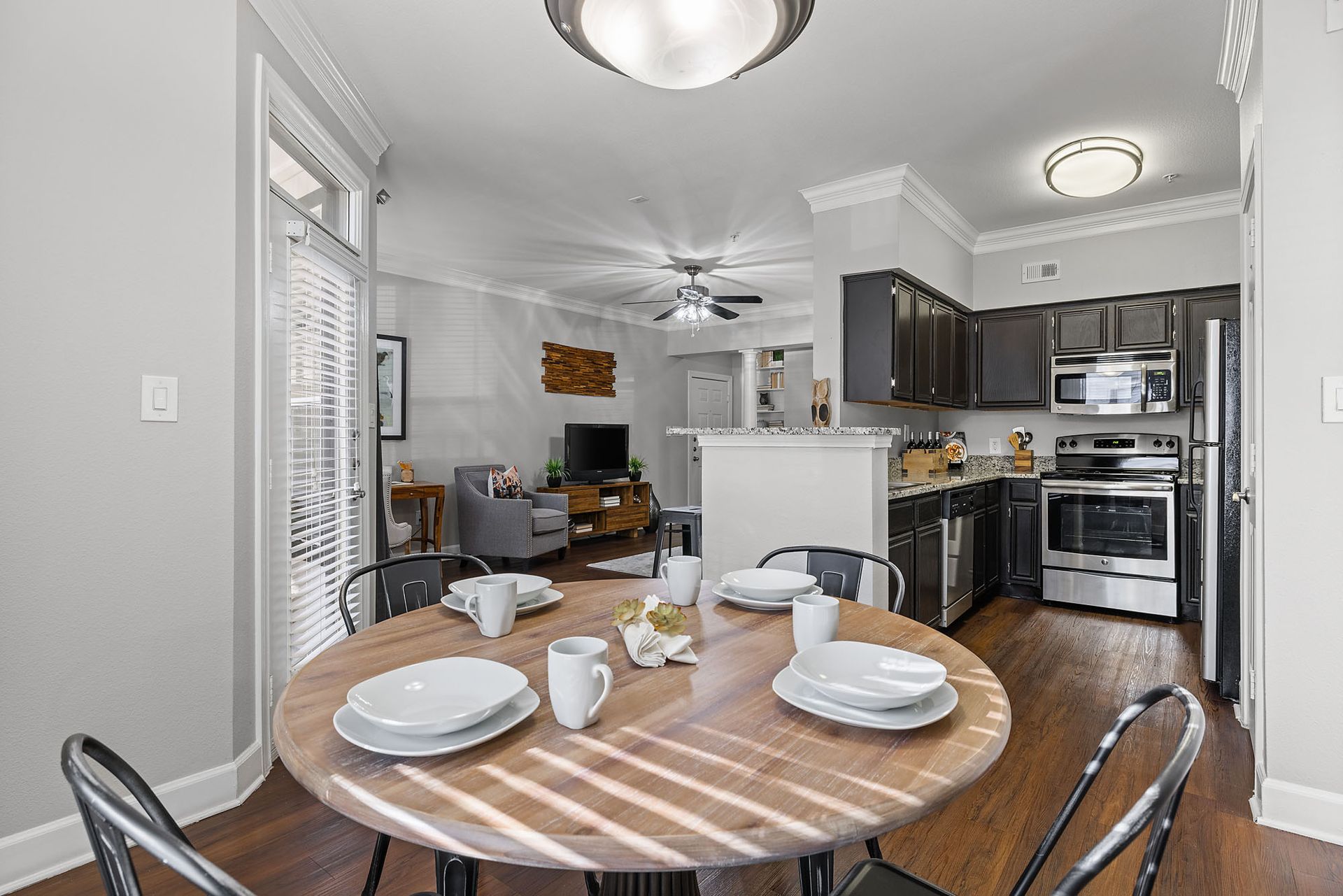 Dining area with round table set for four, open to a gray kitchen and living room in the background at Marquis at Great Hills in Austin, TX.