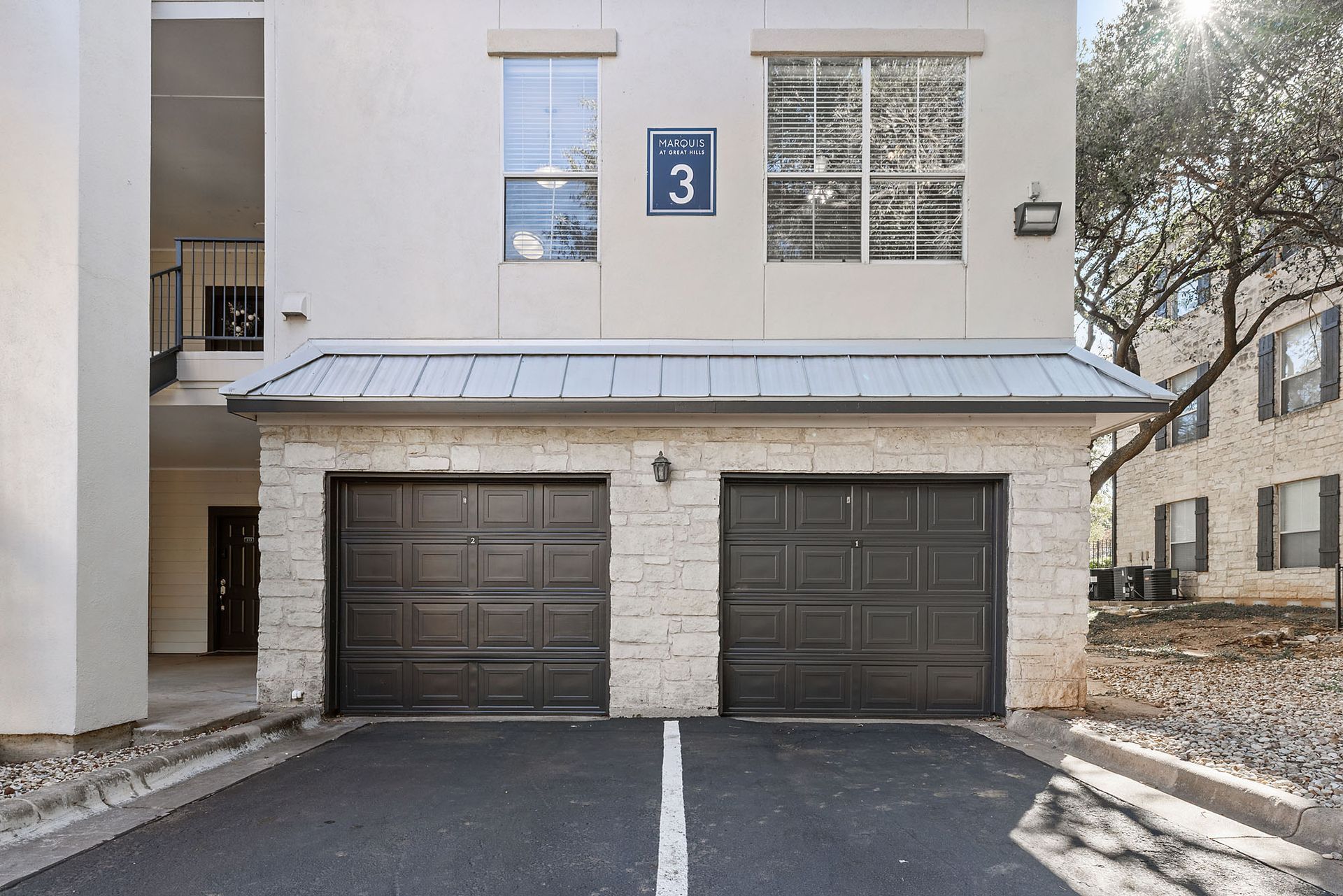 Apartment building entrance with two dark garage doors and a blue number 3 sign above them at Marquis at Great Hills in Austin, TX.