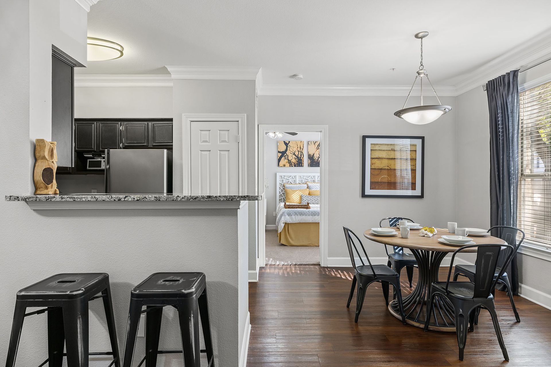 Open kitchen and dining area with barstools, round table, hardwood floors, and sunlight through windows at Marquis at Great Hills in Austin, TX.