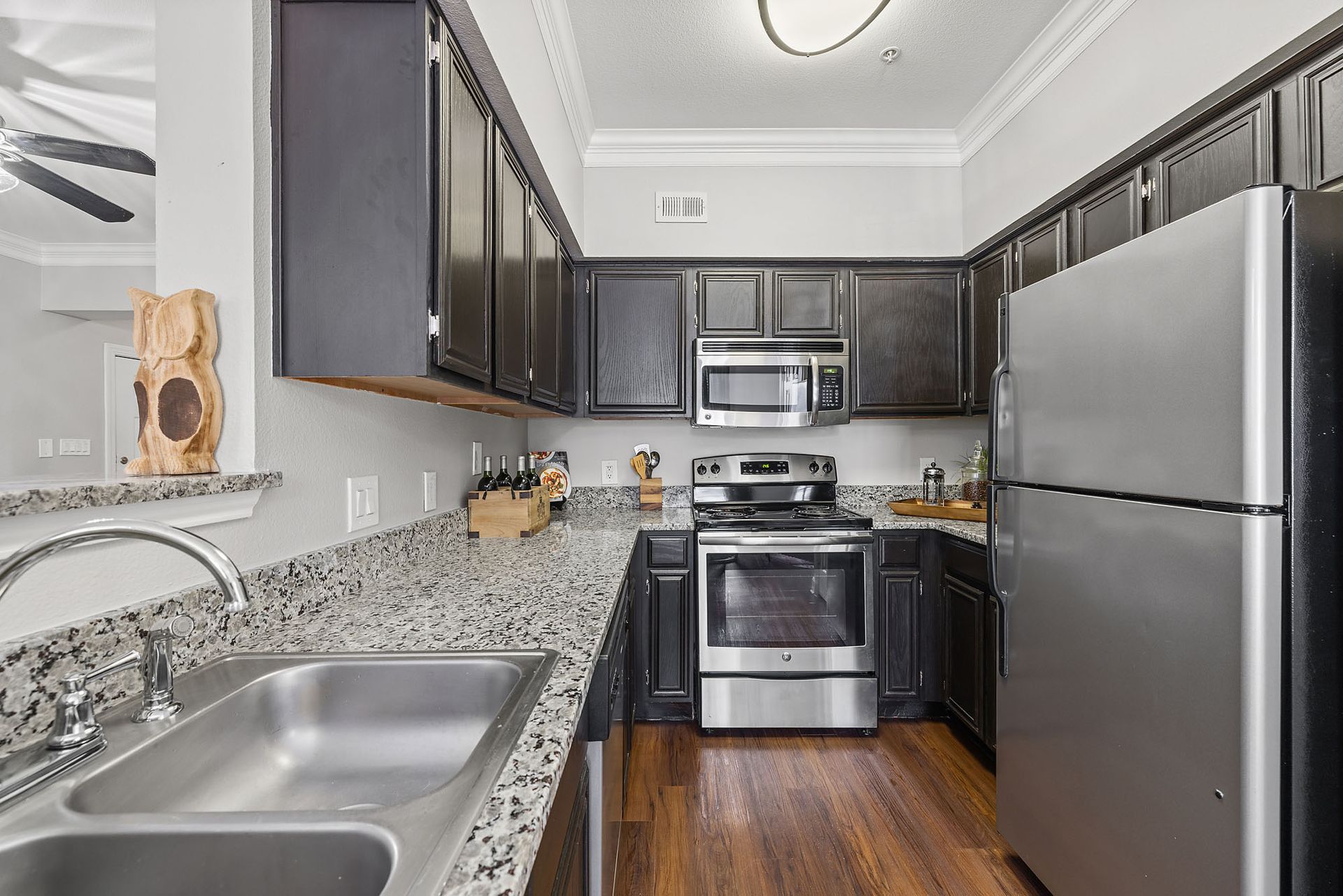 Compact stainless-steel kitchen with dark cabinets, granite counters, and wood floor at Marquis at Great Hills in Austin, TX.