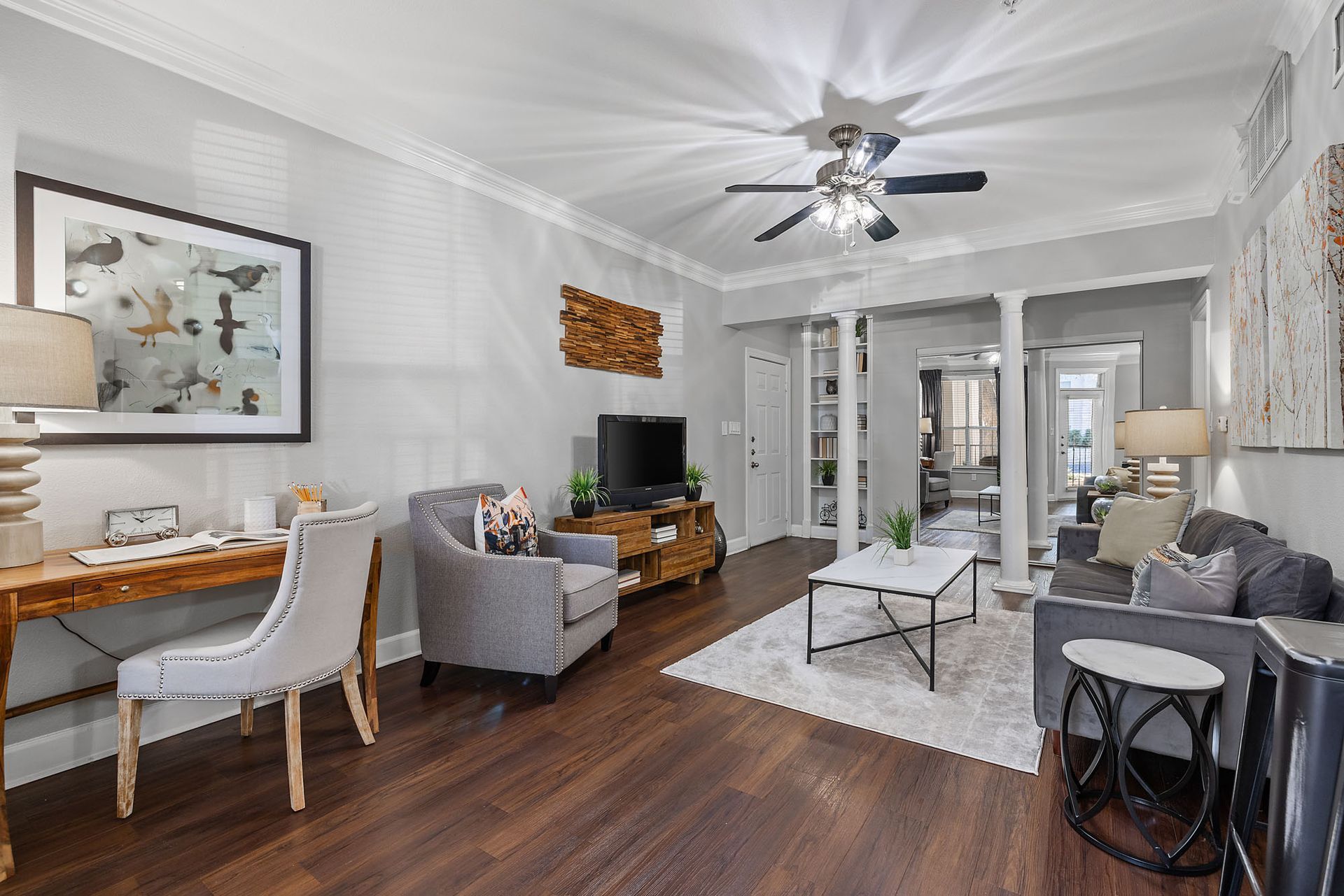 Bright living room with gray sofas, white dining table, dark wood floors, and ceiling fan under a vaulted ceiling at Marquis at Great Hills in Austin, TX.