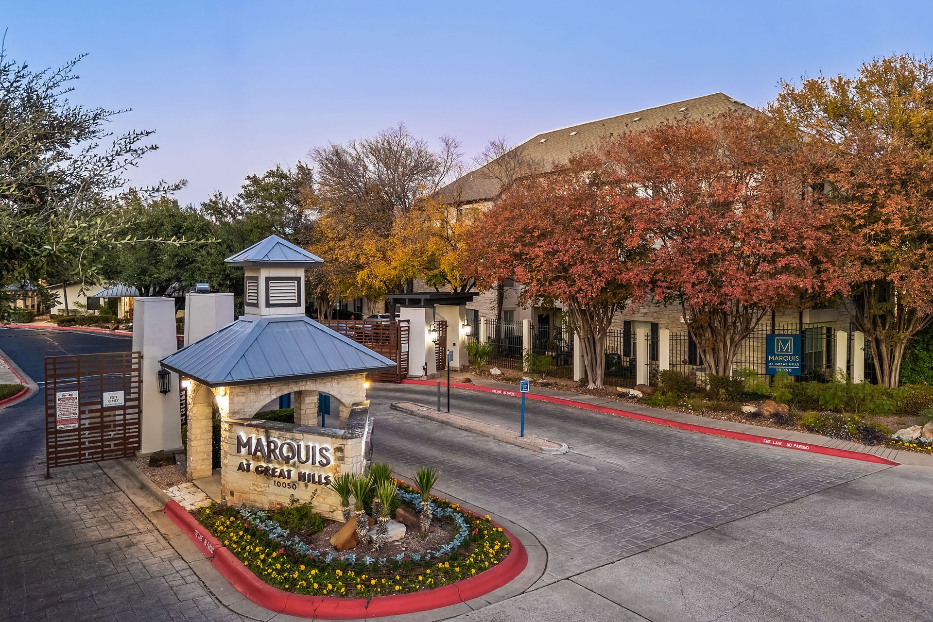 Gatehouse entrance to a residential community with trees and landscaped flower beds at dusk at Marquis at Great Hills in Austin, TX.