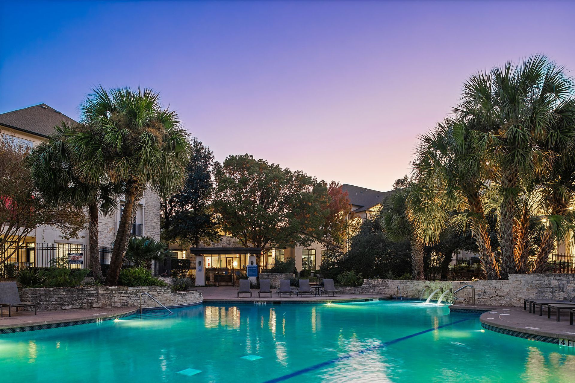 Resort-style pool at dusk with palm trees, lounge chairs, and warm lights reflecting on turquoise water at Marquis at Great Hills in Austin, TX.