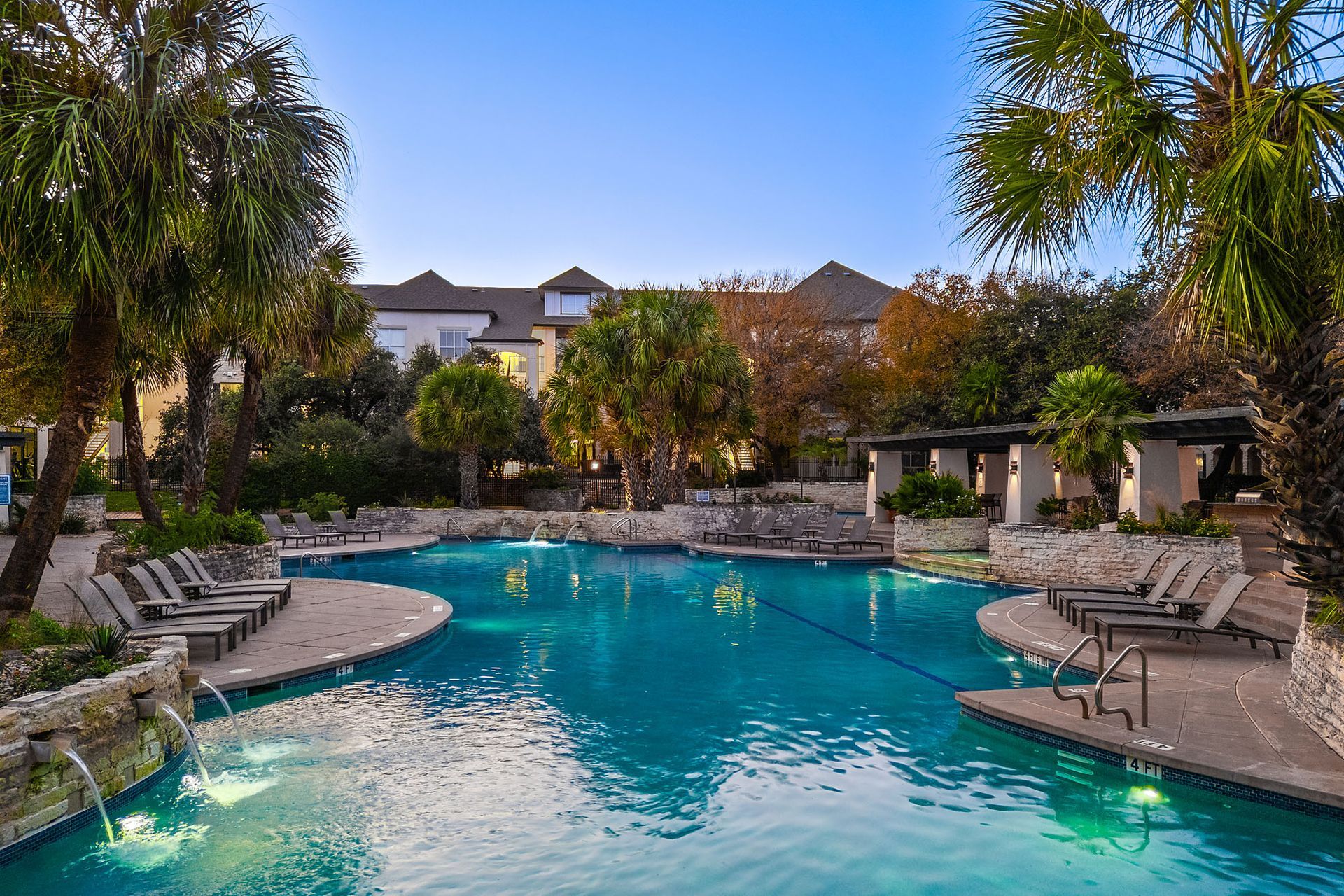 Resort-style outdoor pool with lounge chairs, palm trees, and sunset reflections at Marquis at Great Hills in Austin, TX.