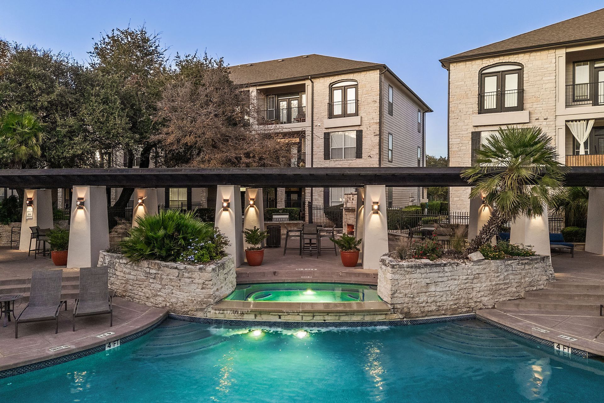 Courtyard pool with turquoise water, lounge chairs, and stone apartment buildings at dusk at Marquis at Great Hills in Austin, TX.