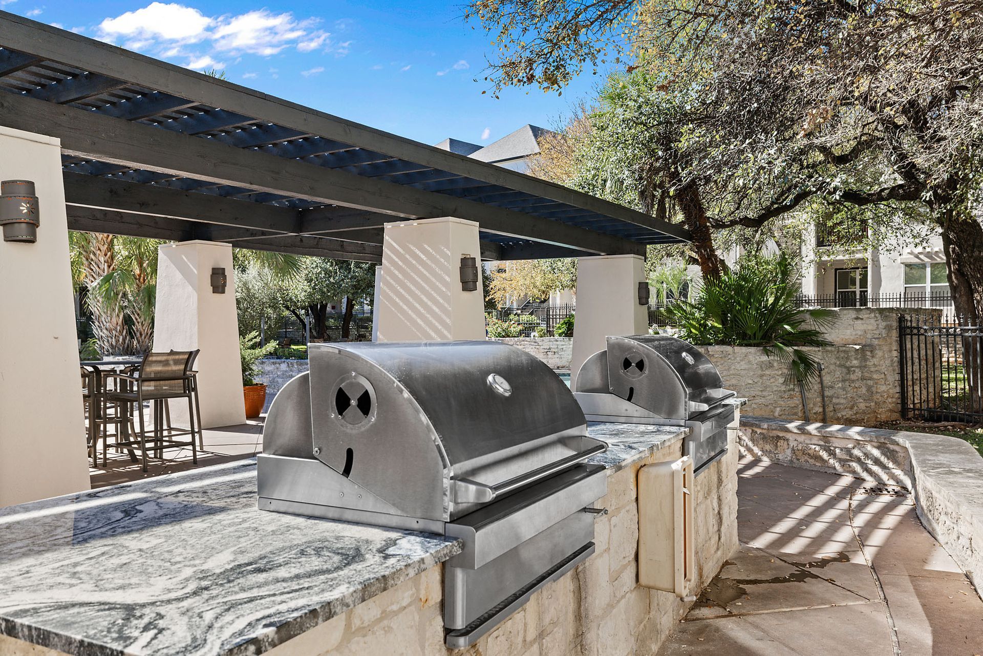 Outdoor stone barbecue grills under a shaded pavilion in a sunny courtyard at Marquis at Great Hills in Austin, TX.