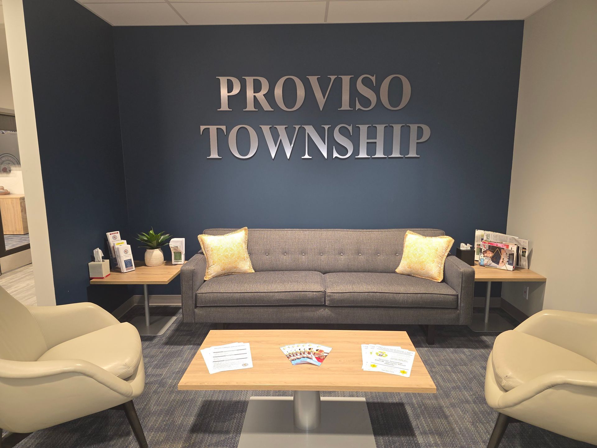 Office waiting area with gray sofa, yellow pillows, blue wall, and