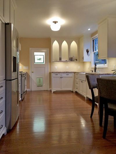A kitchen with hardwood floors , white cabinets and stainless steel appliances.