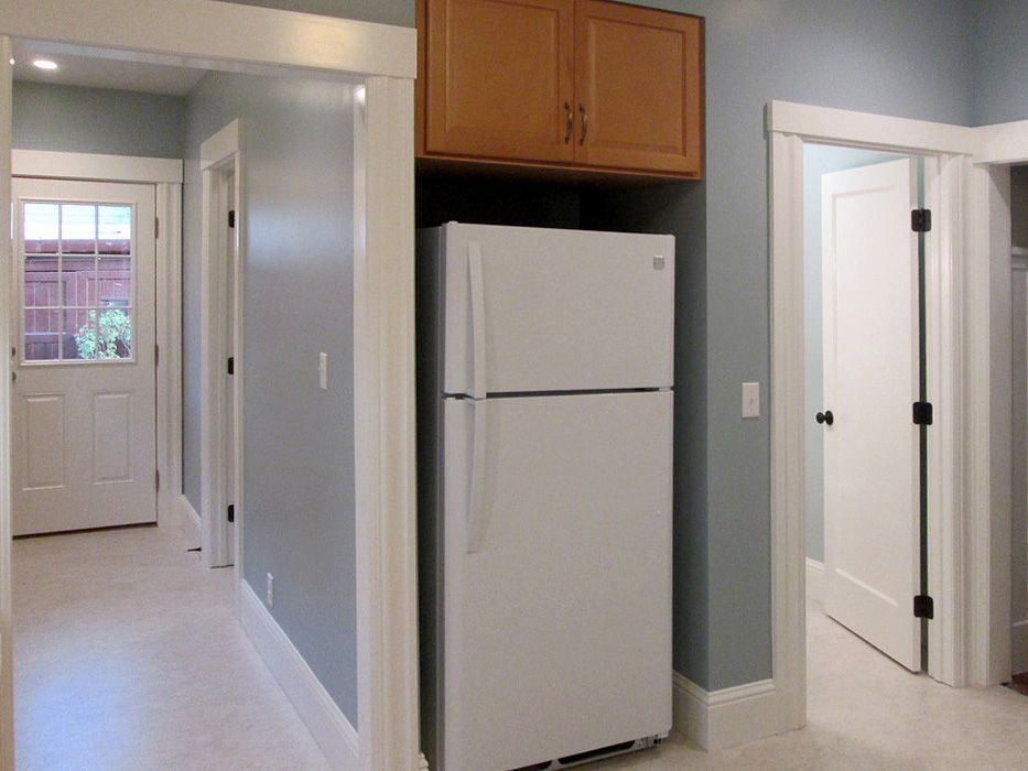 A white refrigerator is sitting in a hallway next to a door.