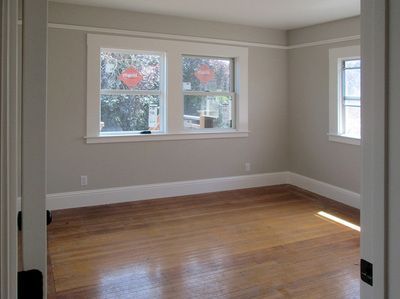 An empty room with hardwood floors and two windows.