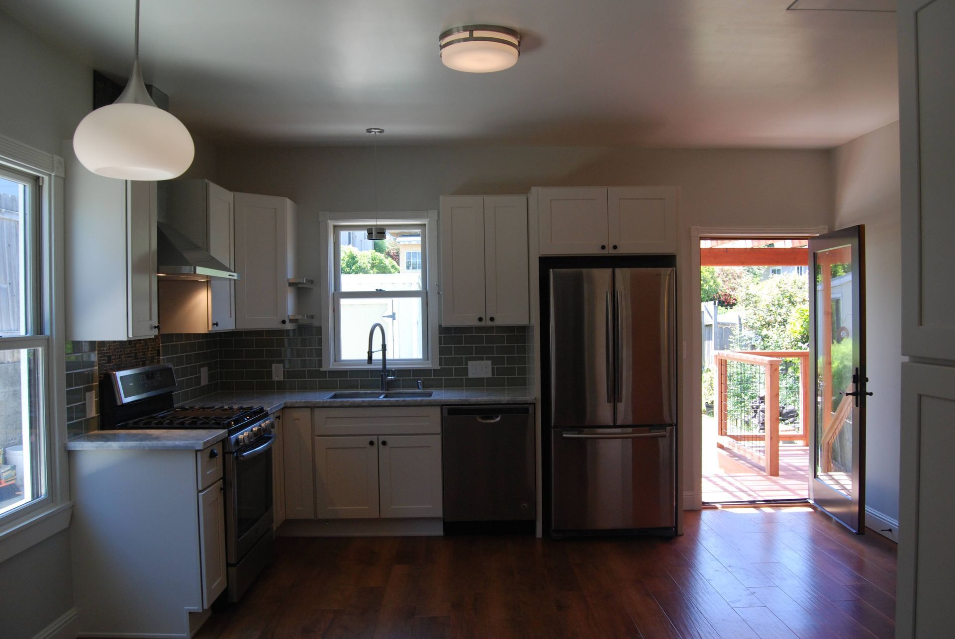 Bright kitchen with stainless steel fridge, white cabinets, and open door to deck.
