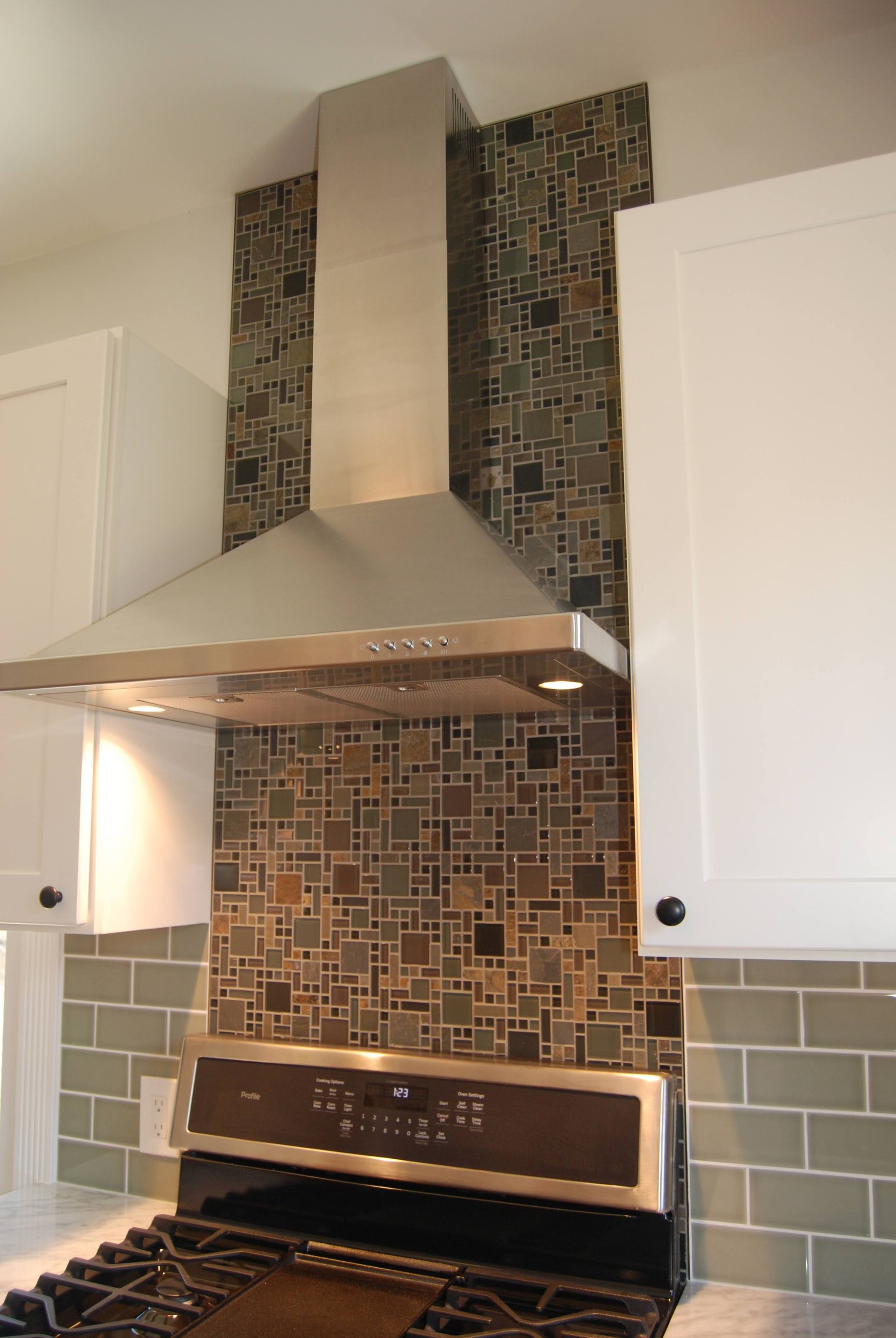 Modern kitchen stove with stainless range hood and mosaic tile backsplash