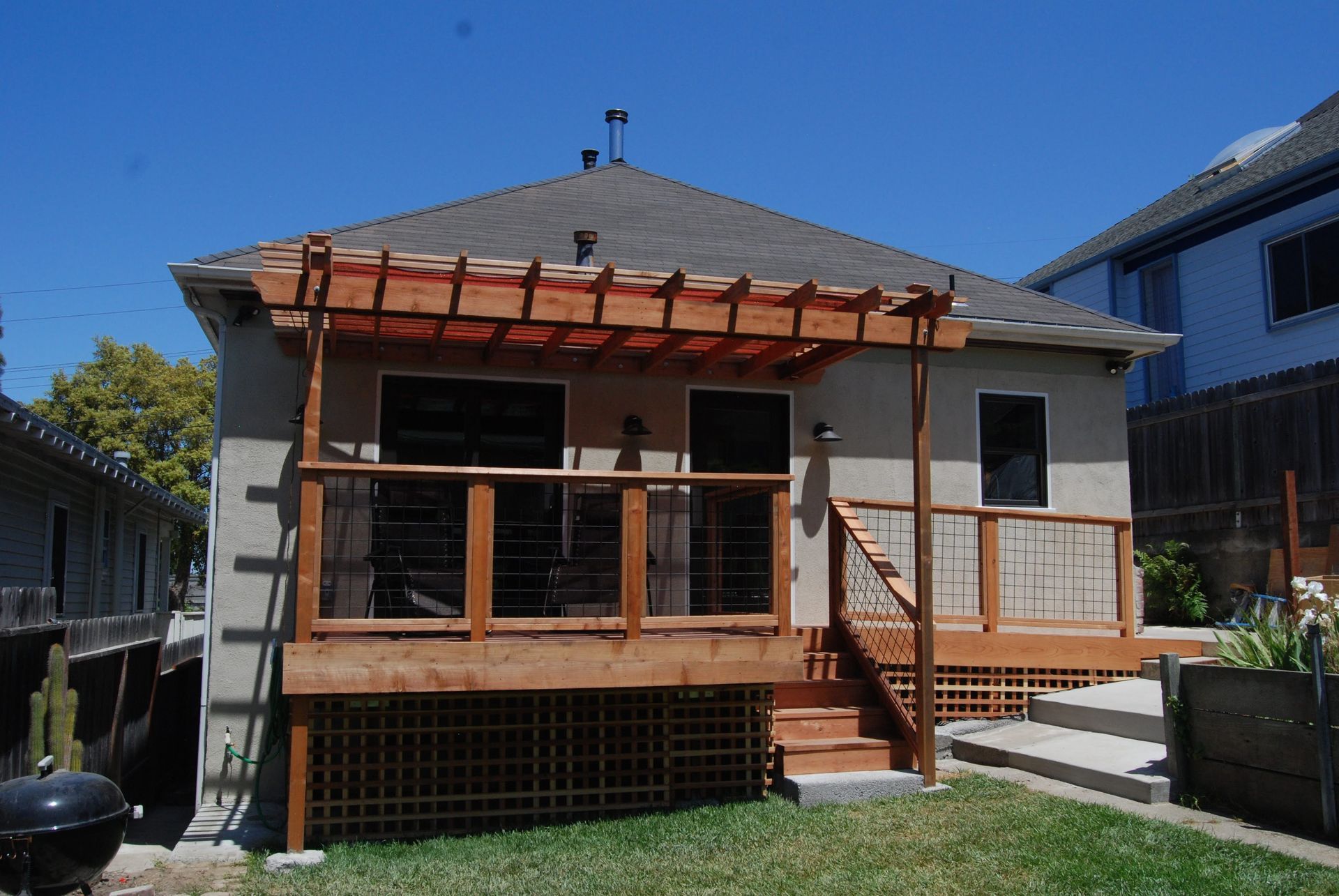 Small house with a wooden porch and railings, red trim, and a grassy yard on a sunny day