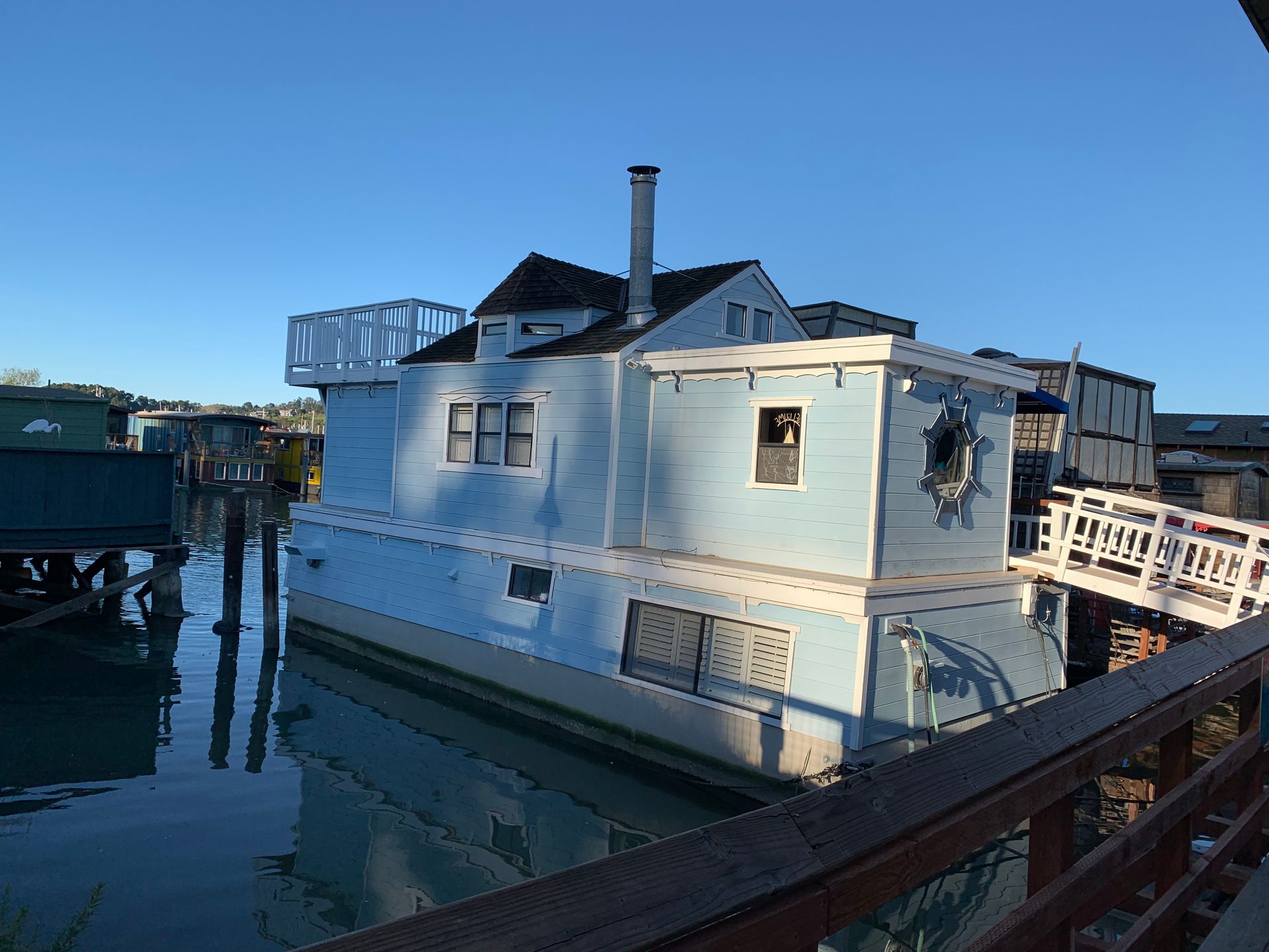 White houseboat docked on calm water at sunset, with a bridge and railing in the foreground.
