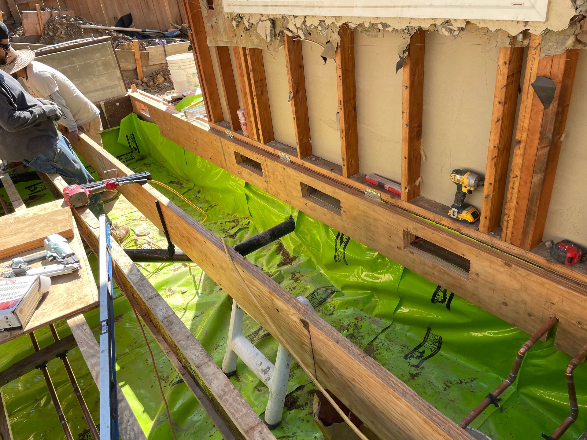 Workers installing bright green waterproofing on a house foundation during construction