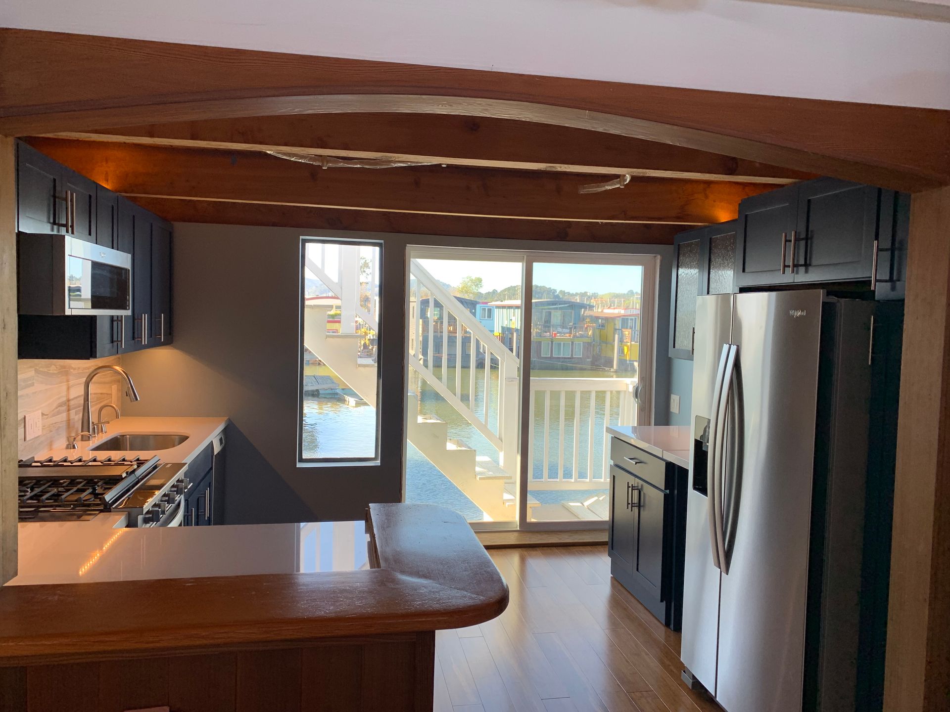 Modern kitchen with dark cabinets, stainless steel appliances, wood ceiling, and sliding glass door to a deck.