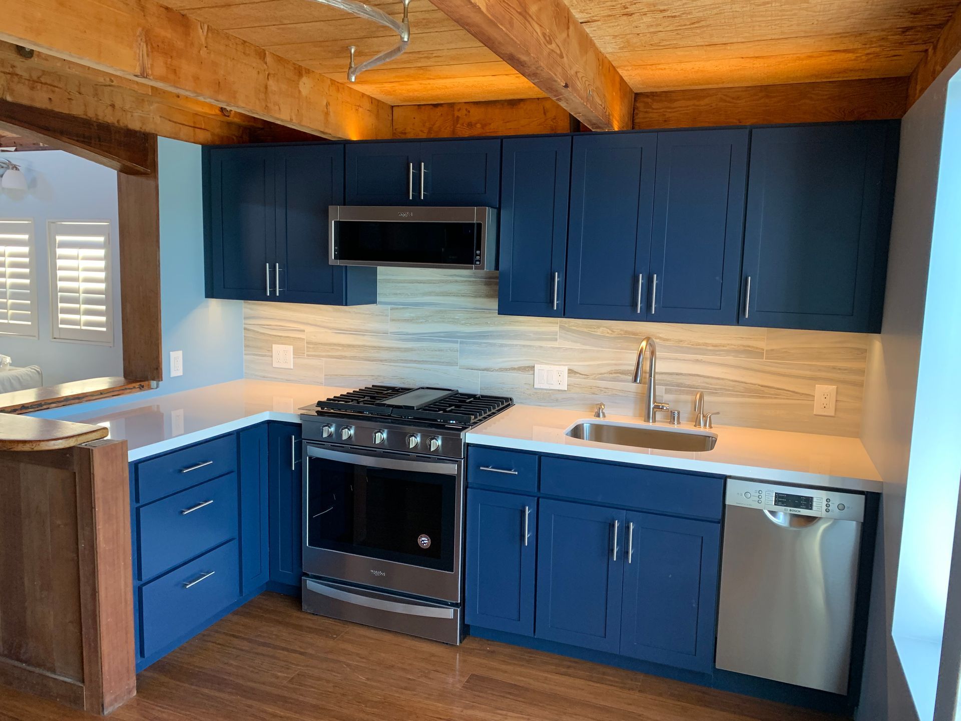 Modern kitchen with blue cabinets, stainless appliances, white tile backsplash, and wood ceiling.