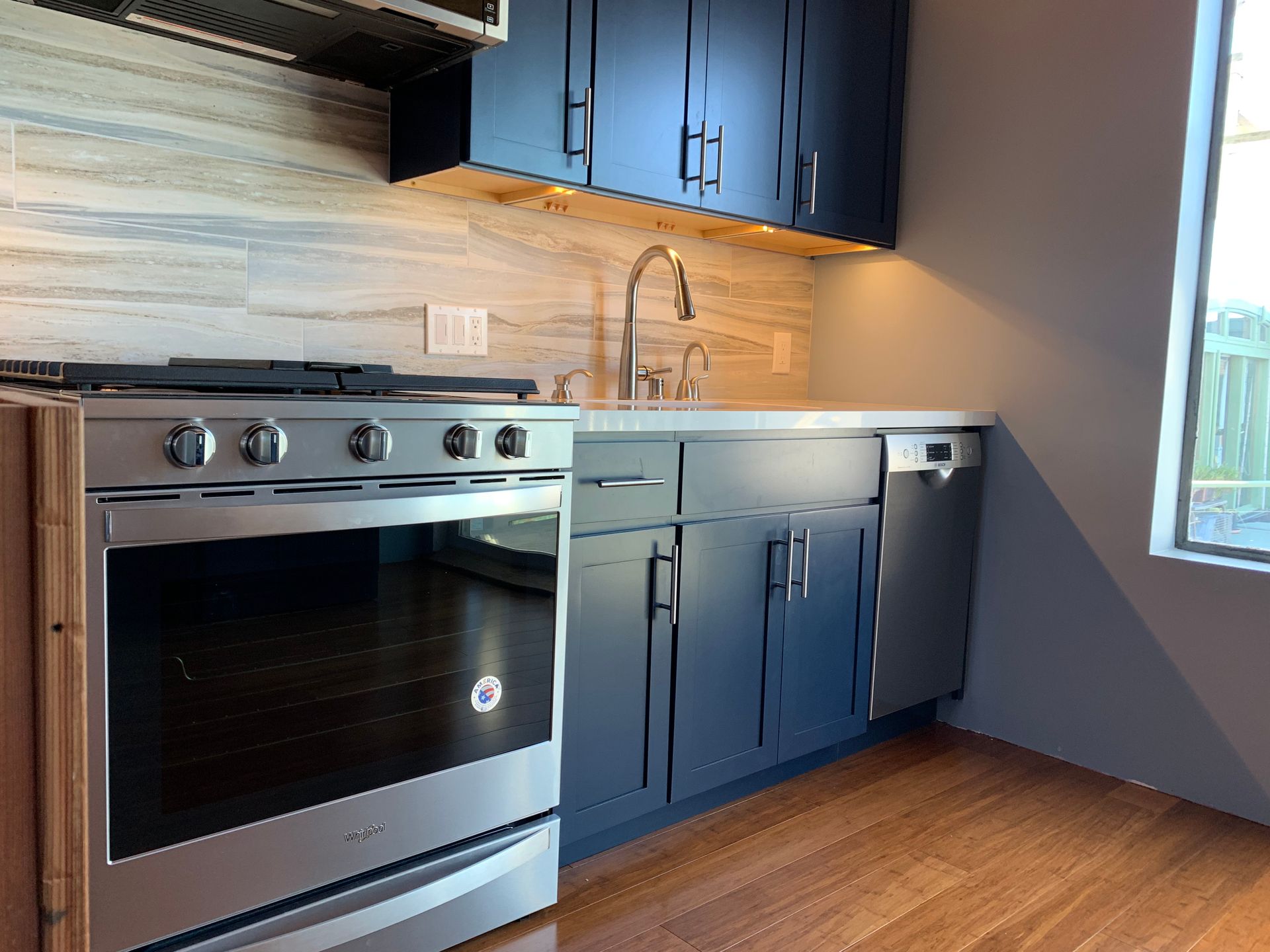 Modern kitchen with stainless steel stove, blue cabinets, wood backsplash, and hardwood floor.