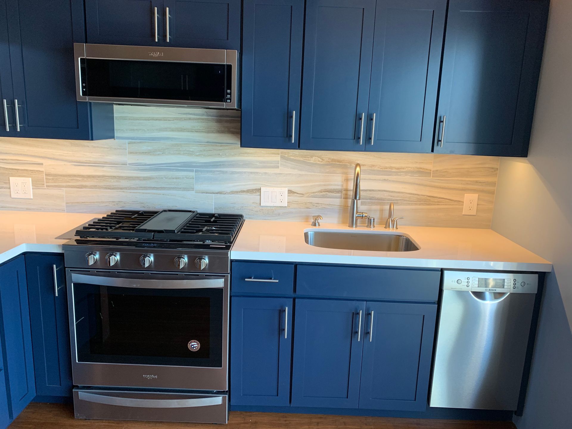 Blue kitchen with stainless steel stove, microwave, sink, and dishwasher under blue cabinets.