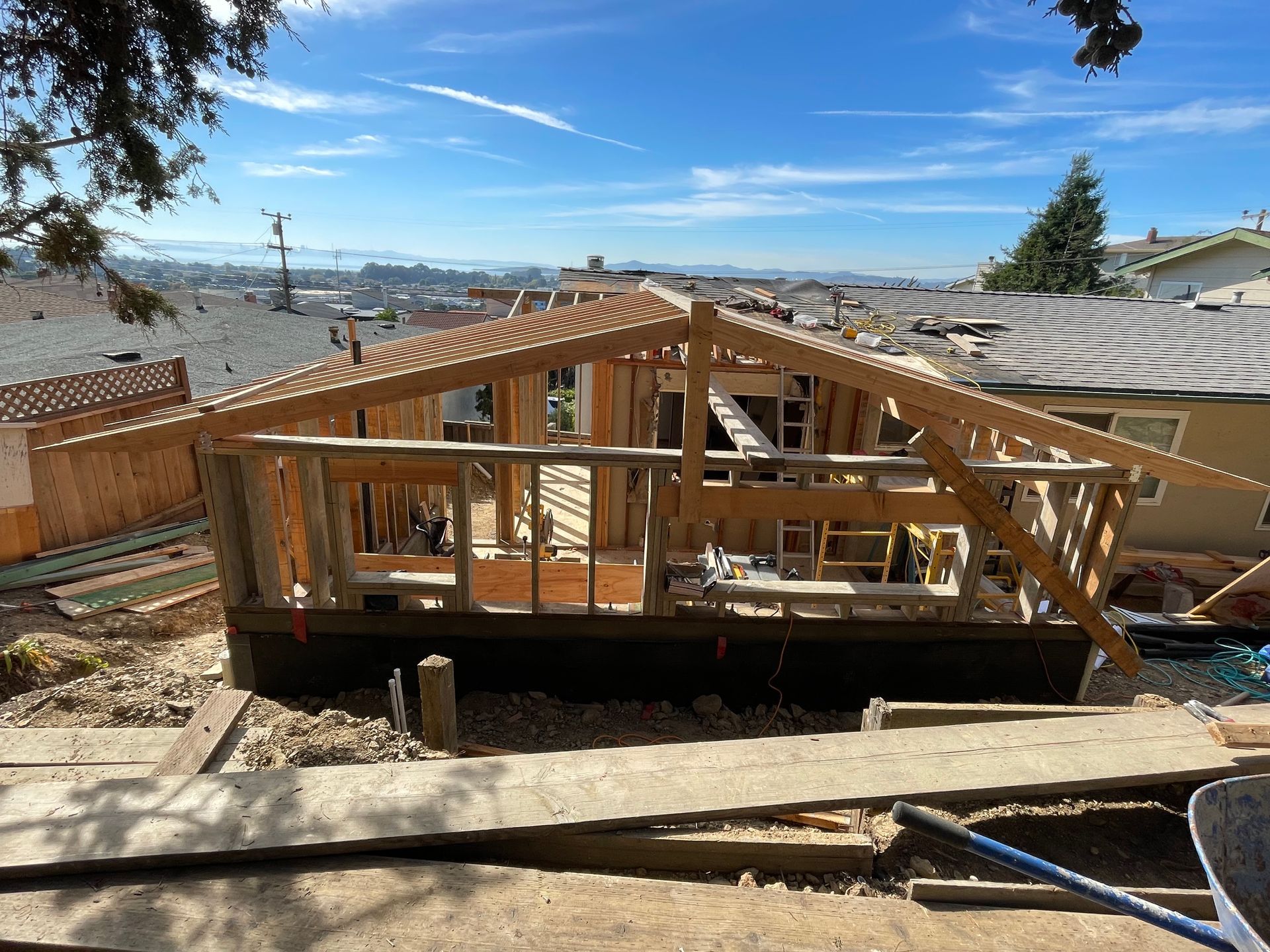 Wood-framed house under construction on a hillside with city views and a clear blue sky