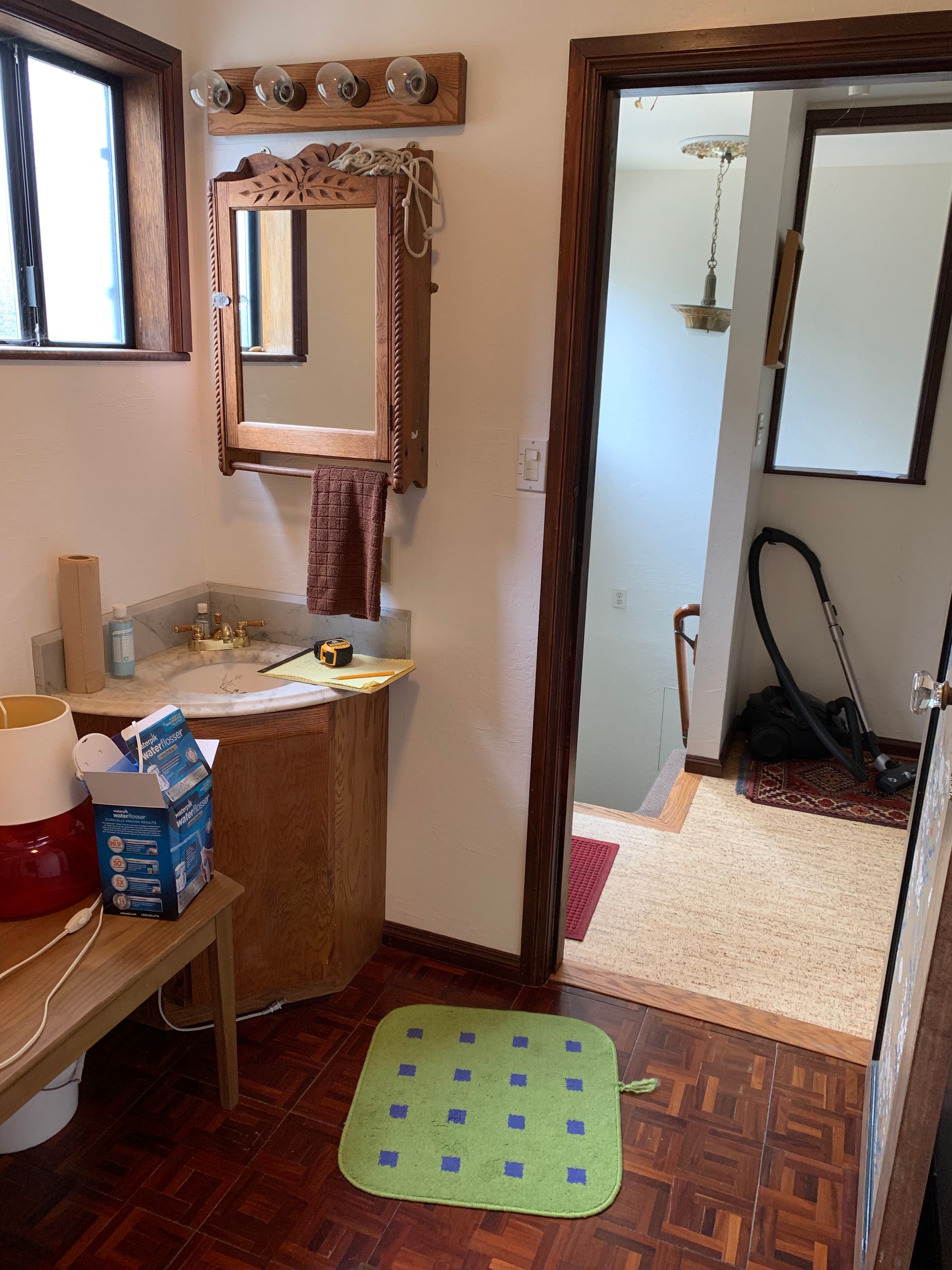 Small bathroom with sink, mirror, doorway, and green bath mat on parquet floor.