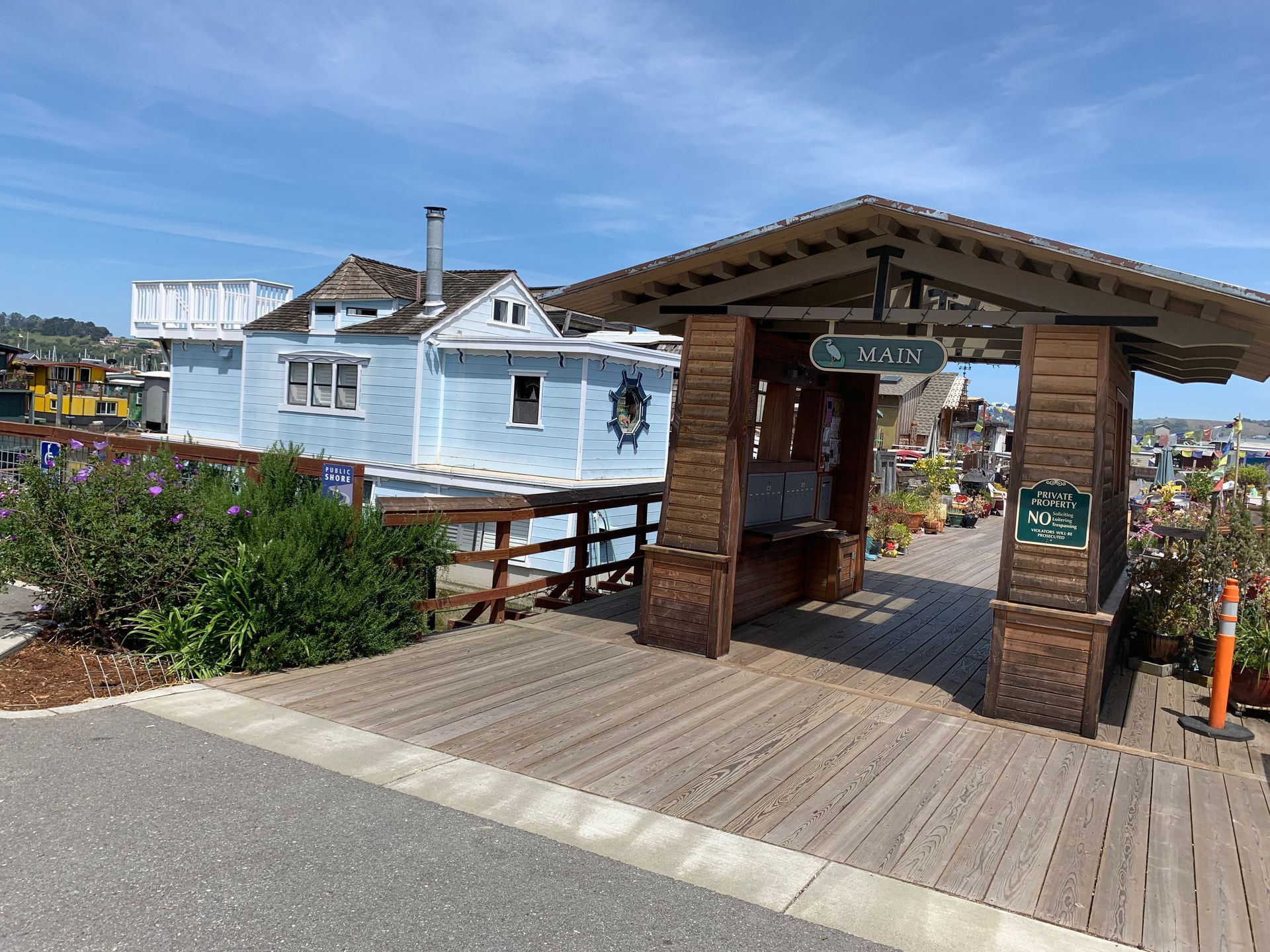 Wooden boardwalk entrance with a small shelter overlooking the water and blue seaside buildings