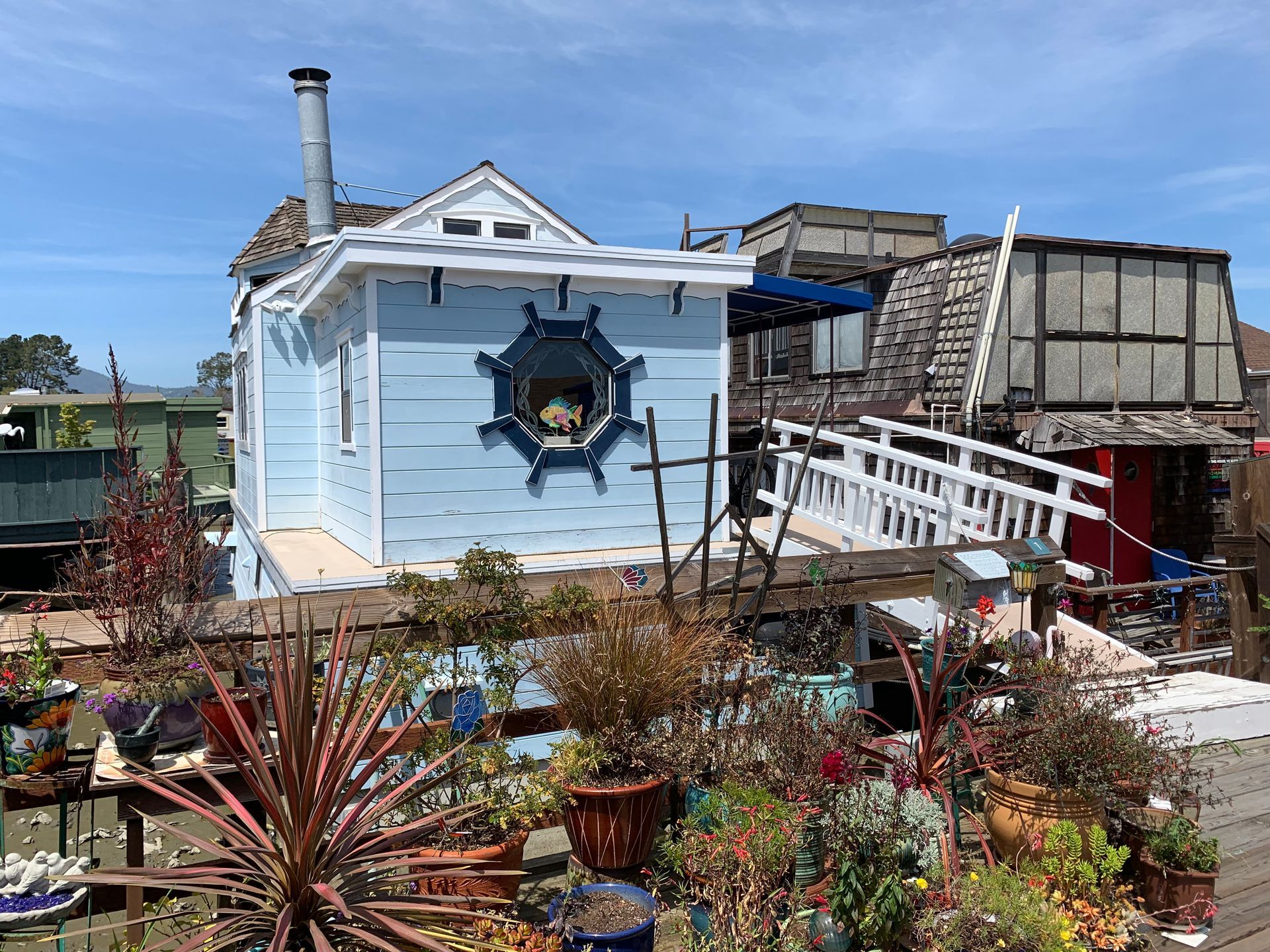 Light blue house with a star-shaped window, white ramp, and colorful potted garden in front