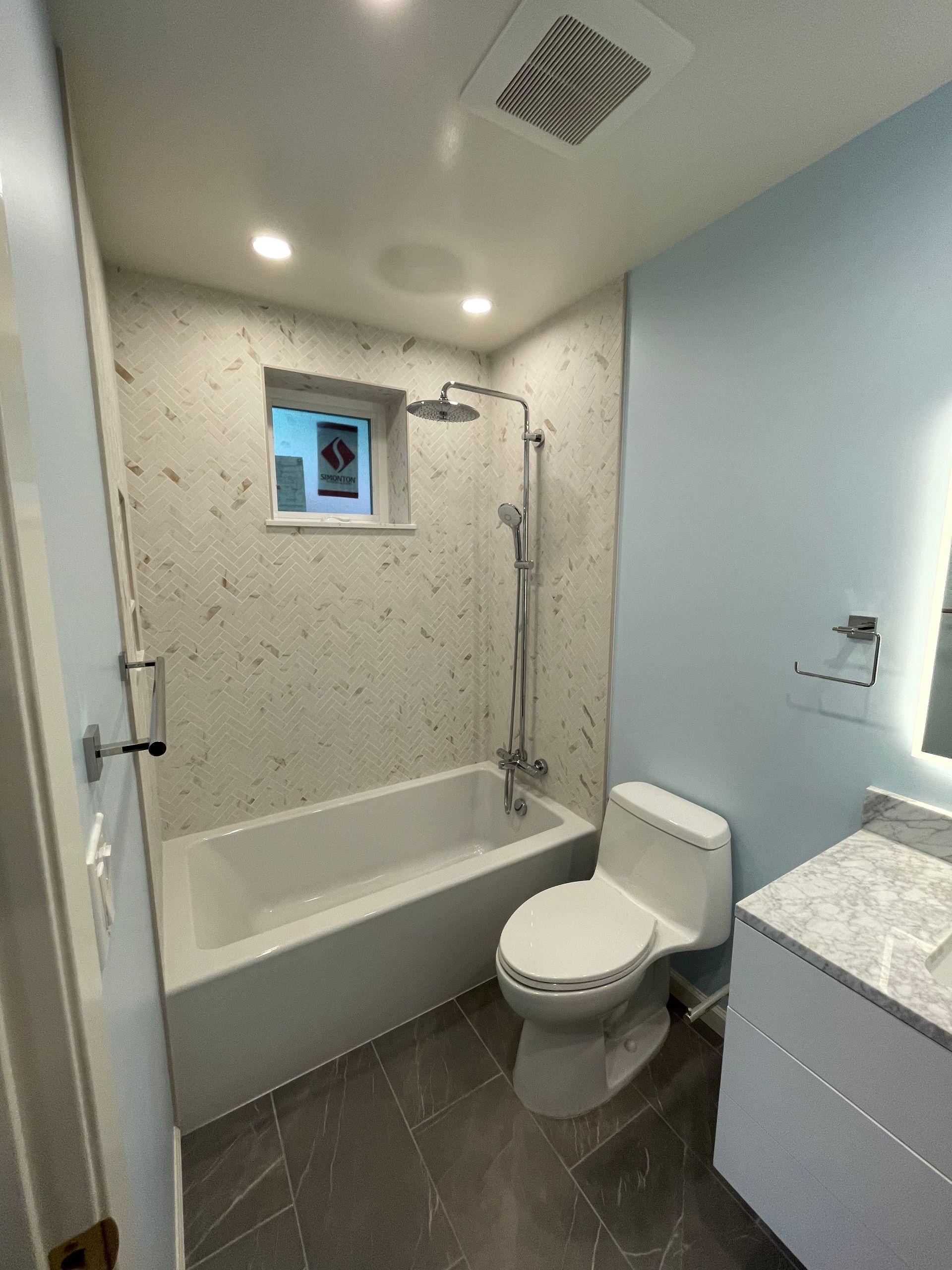 Small modern bathroom with bathtub, shower, toilet, and light blue walls