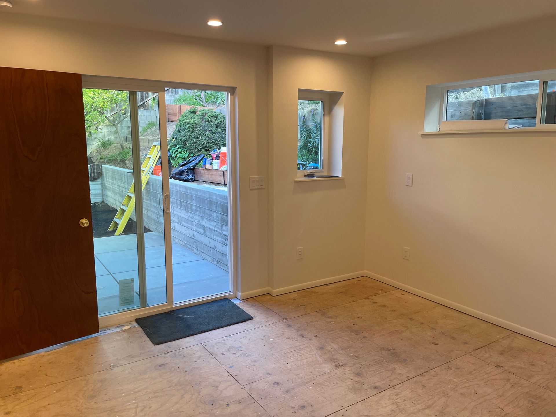 Empty room with wood floor, open front door, and windows overlooking a patio.