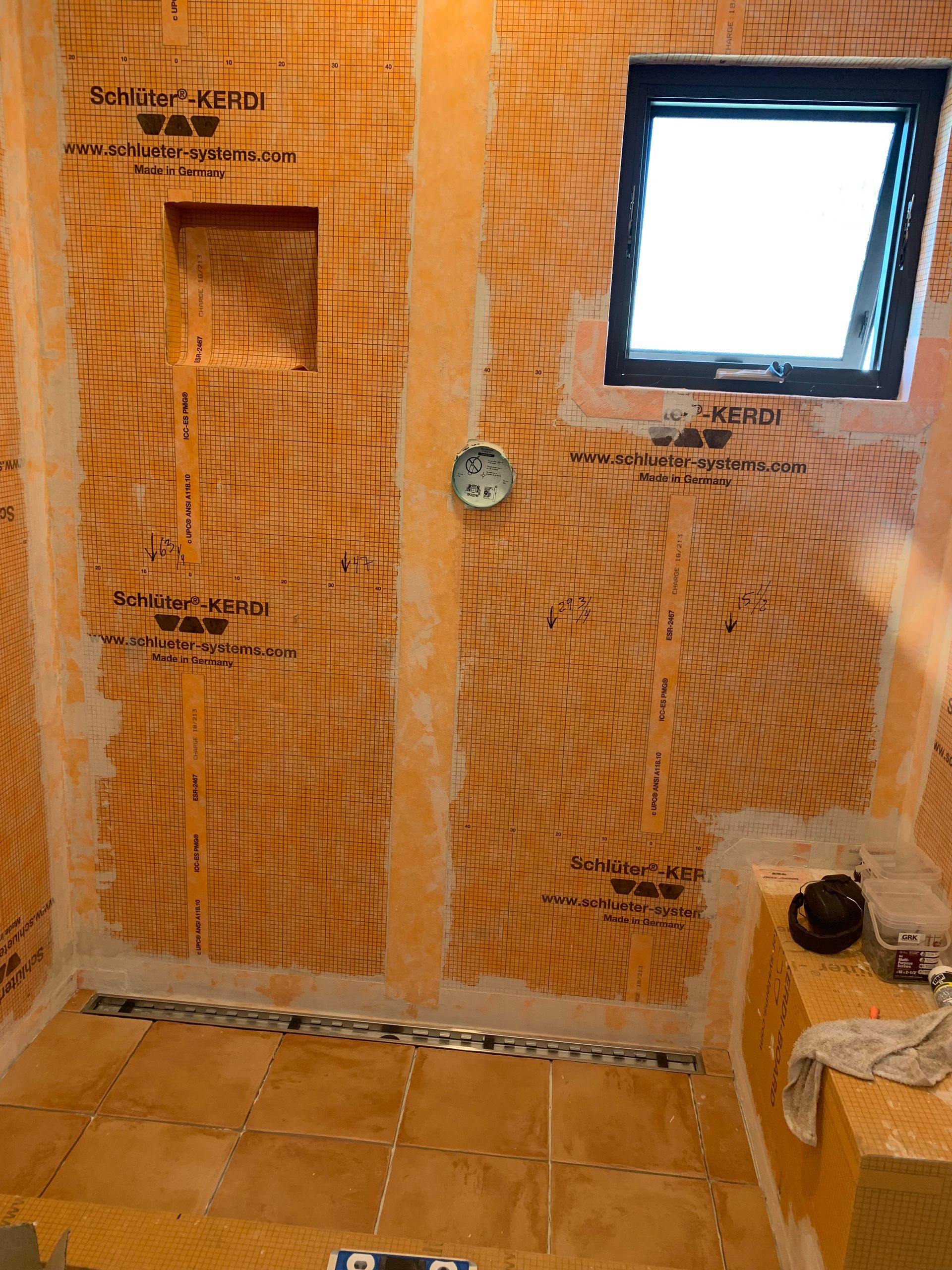 Orange waterproofed bathroom under renovation with tiled walls, a window, and exposed plumbing outlet