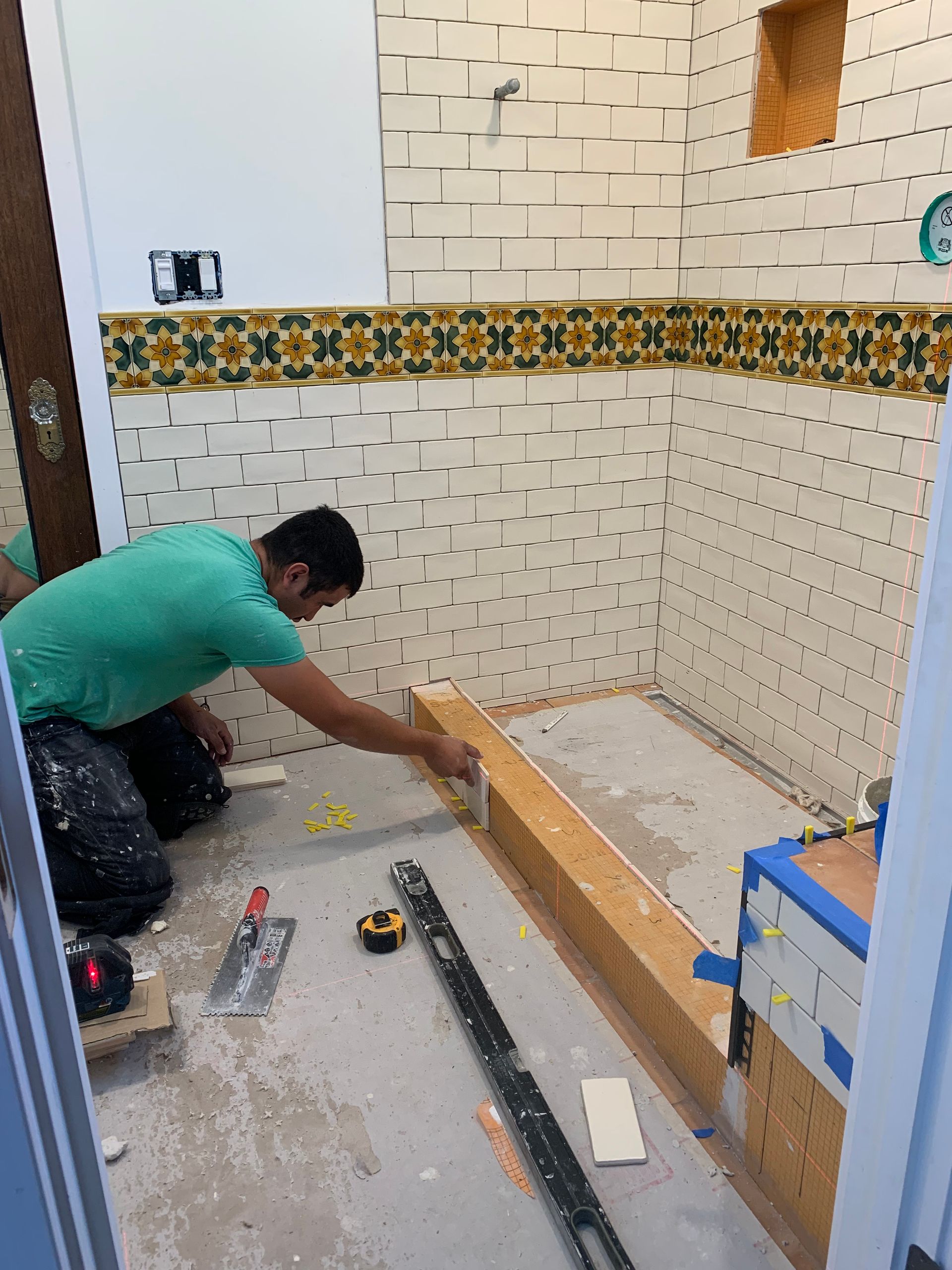 Worker installing a wooden base in a tiled room under renovation