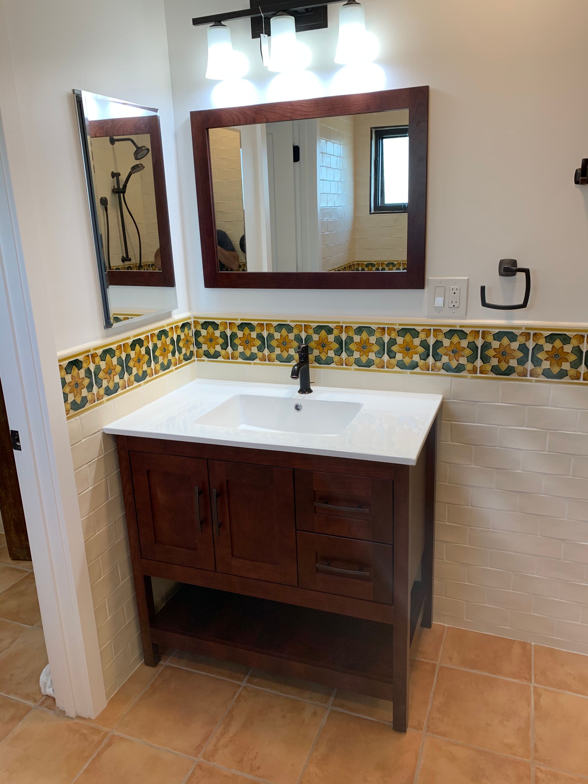 Bathroom vanity with wood cabinet, white sink, and mirror above decorative tile border.