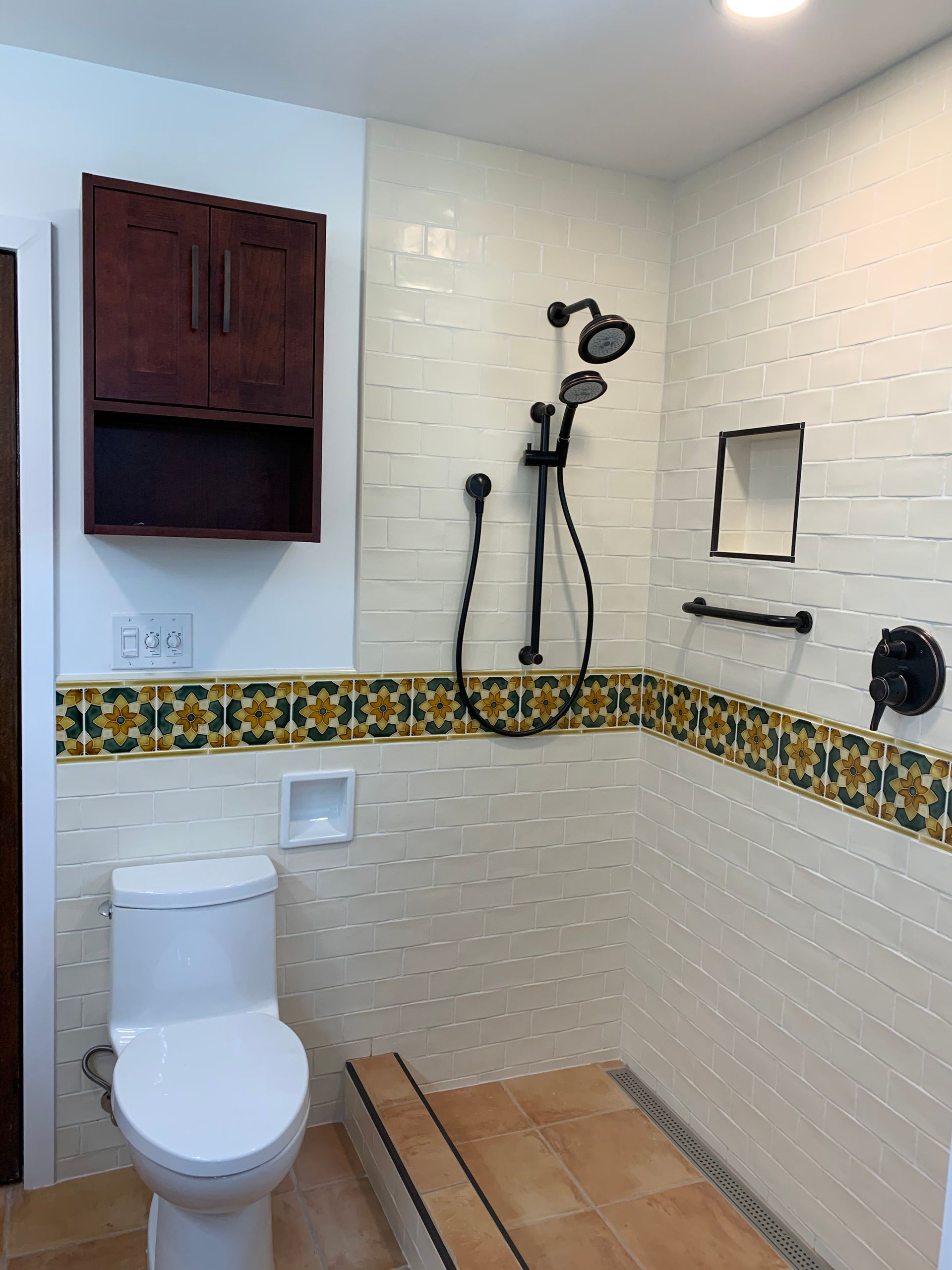 Accessible bathroom with toilet, wall-mounted shower, grab bar, and tiled bench area.