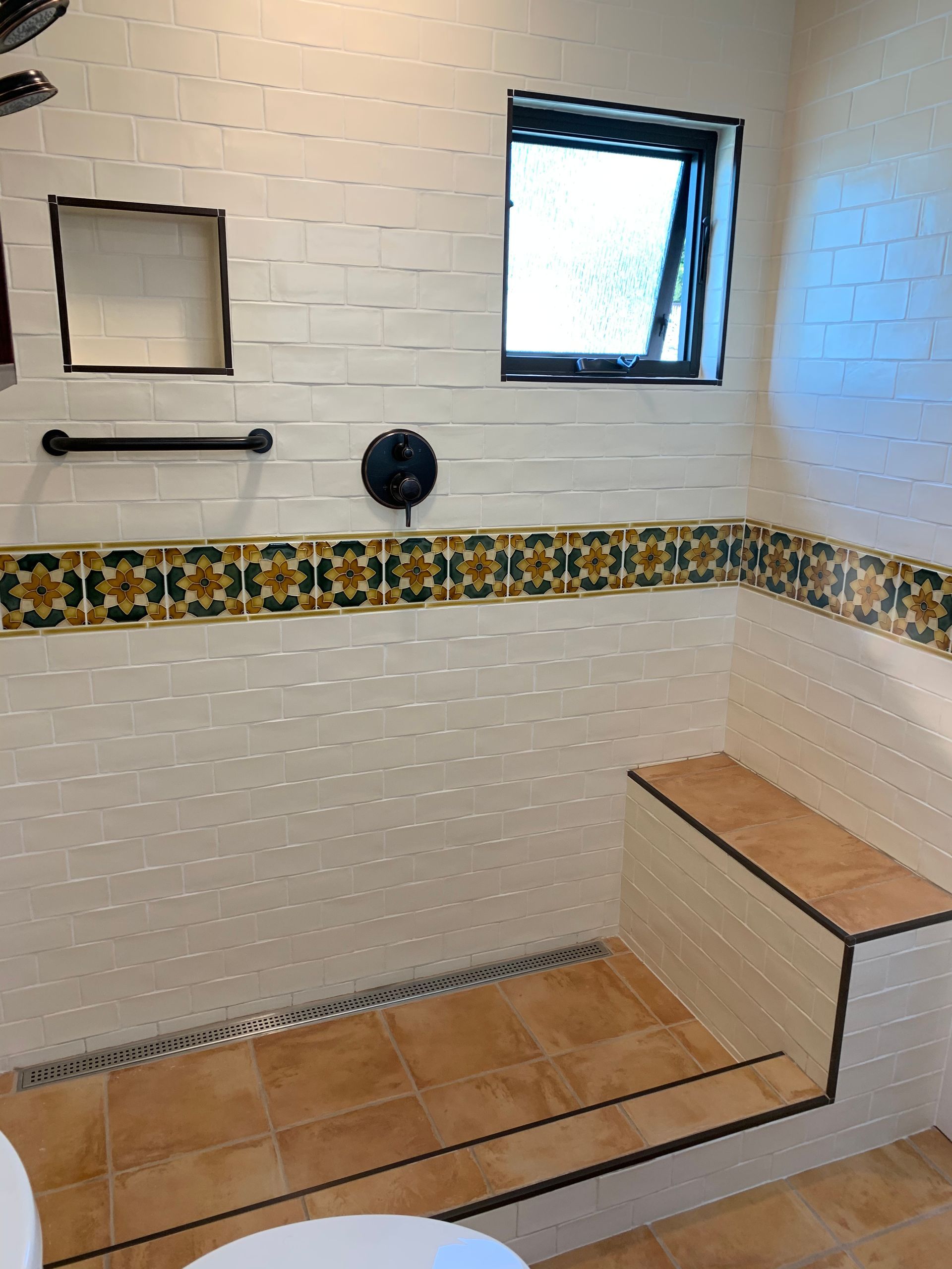 Accessible tiled shower with bench, grab bar, window, and decorative mosaic border.
