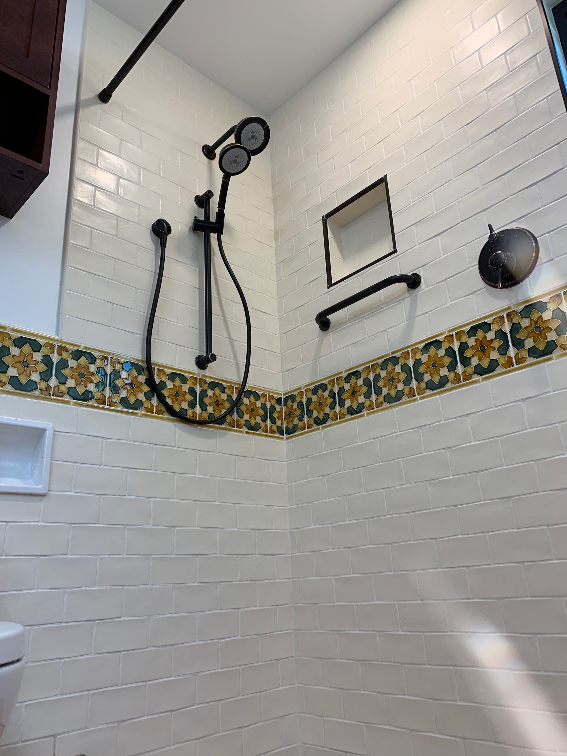 Walk-in shower with white tile, blue floral border, handheld showerhead, and hanging storage shelves.