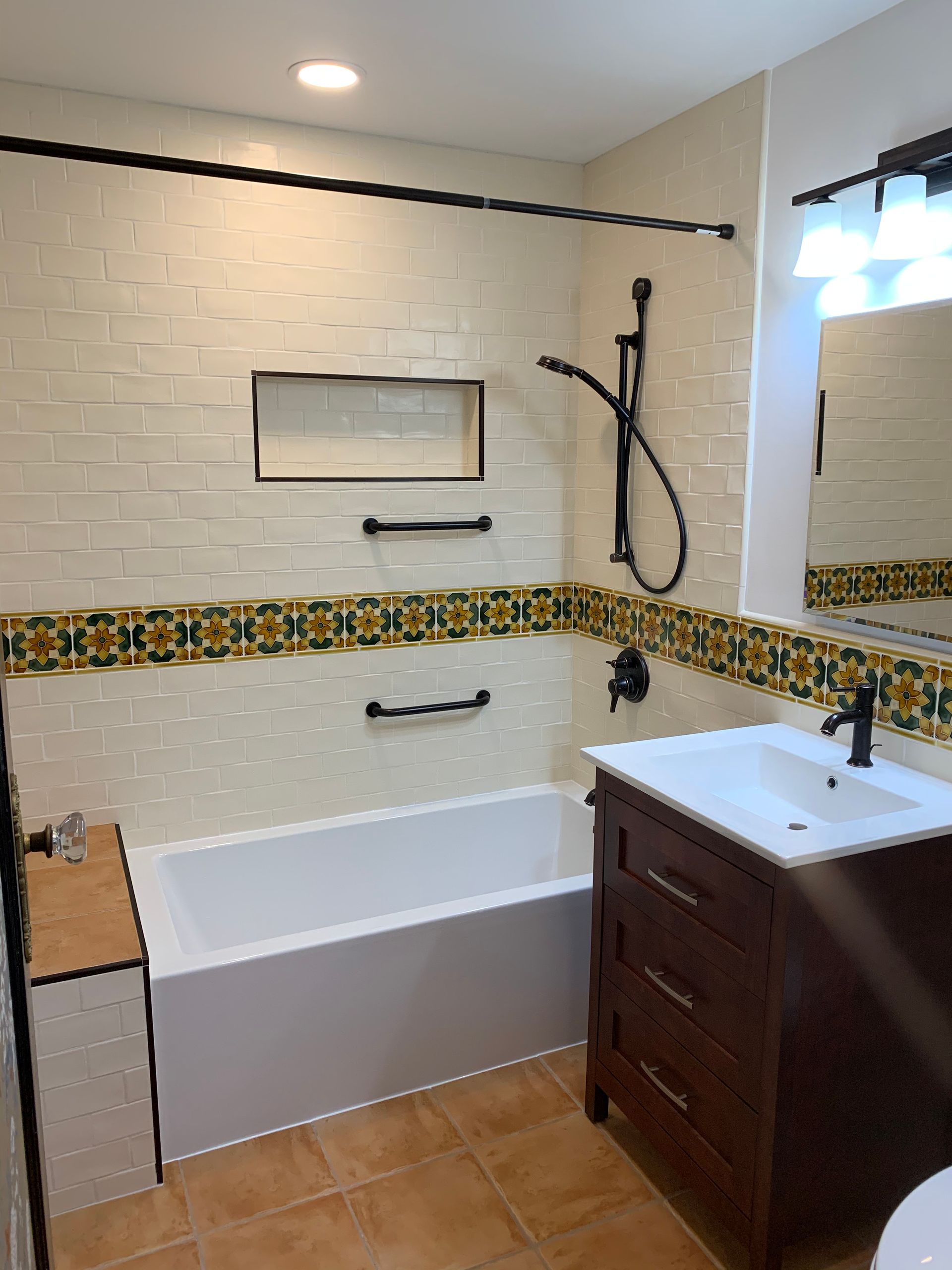 Bathroom with bathtub, vanity, and showerhead, featuring white tile and colorful mosaic trim.