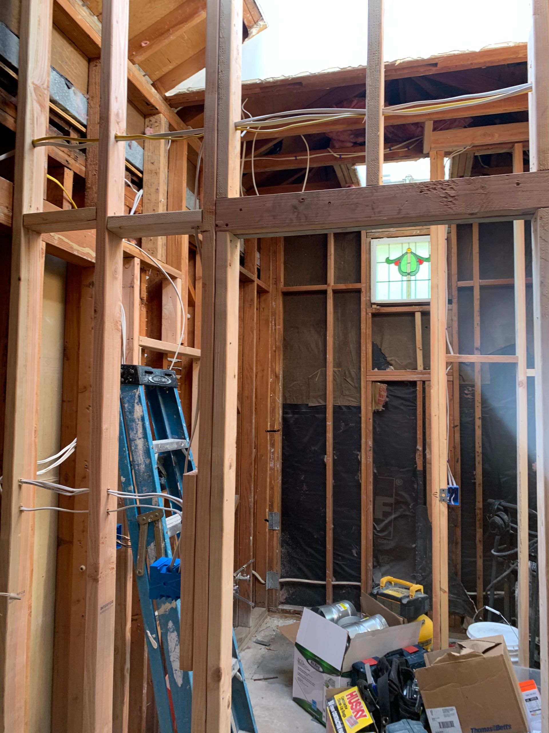 Unfinished house interior with exposed wood framing, a ladder, and construction materials scattered on the floor.