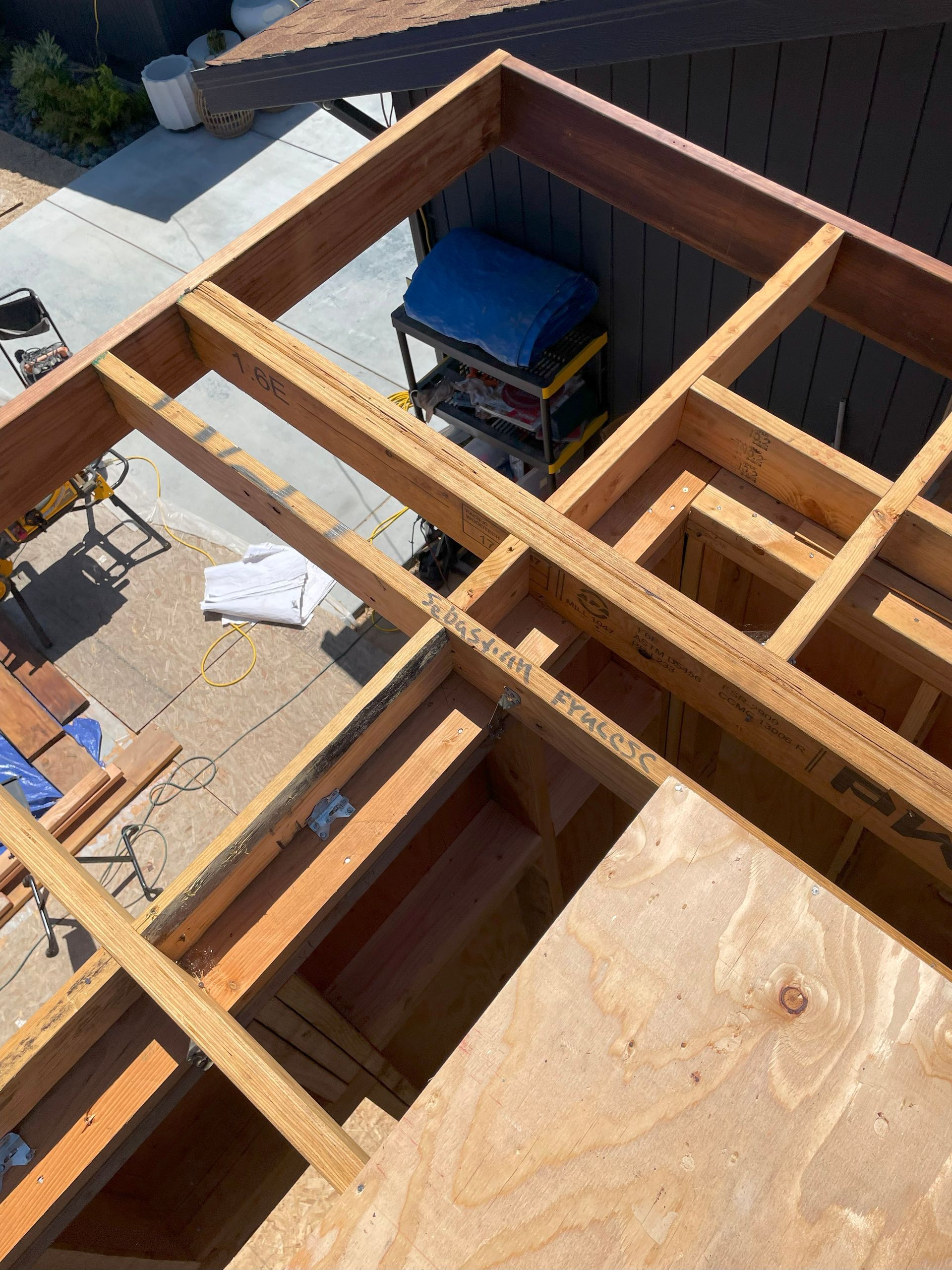 Rooftop under construction with exposed wooden framing, plywood, and a blue tool bag under the roof opening