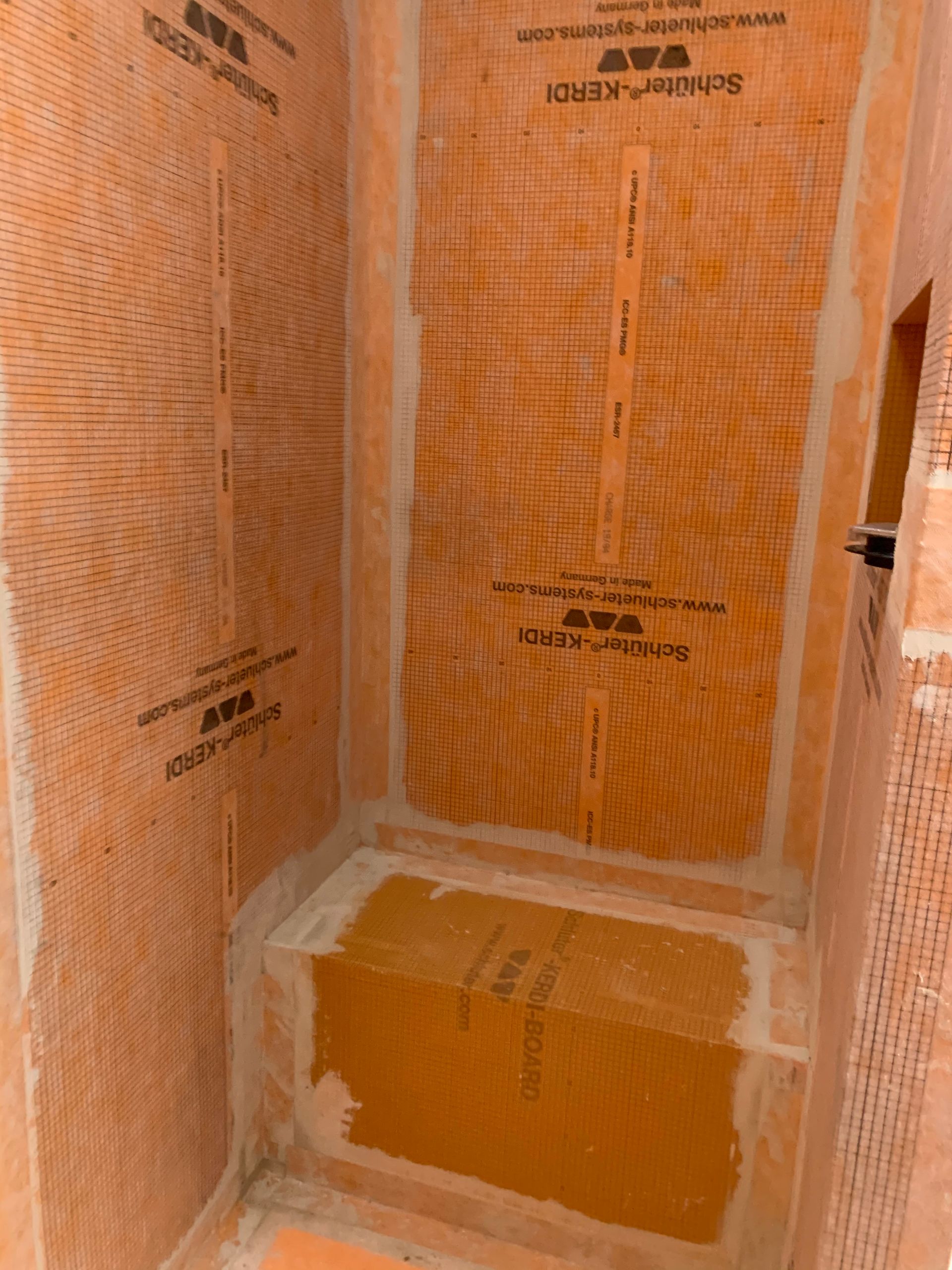 Orange waterproofed shower stall interior with a built-in bench and tiled walls