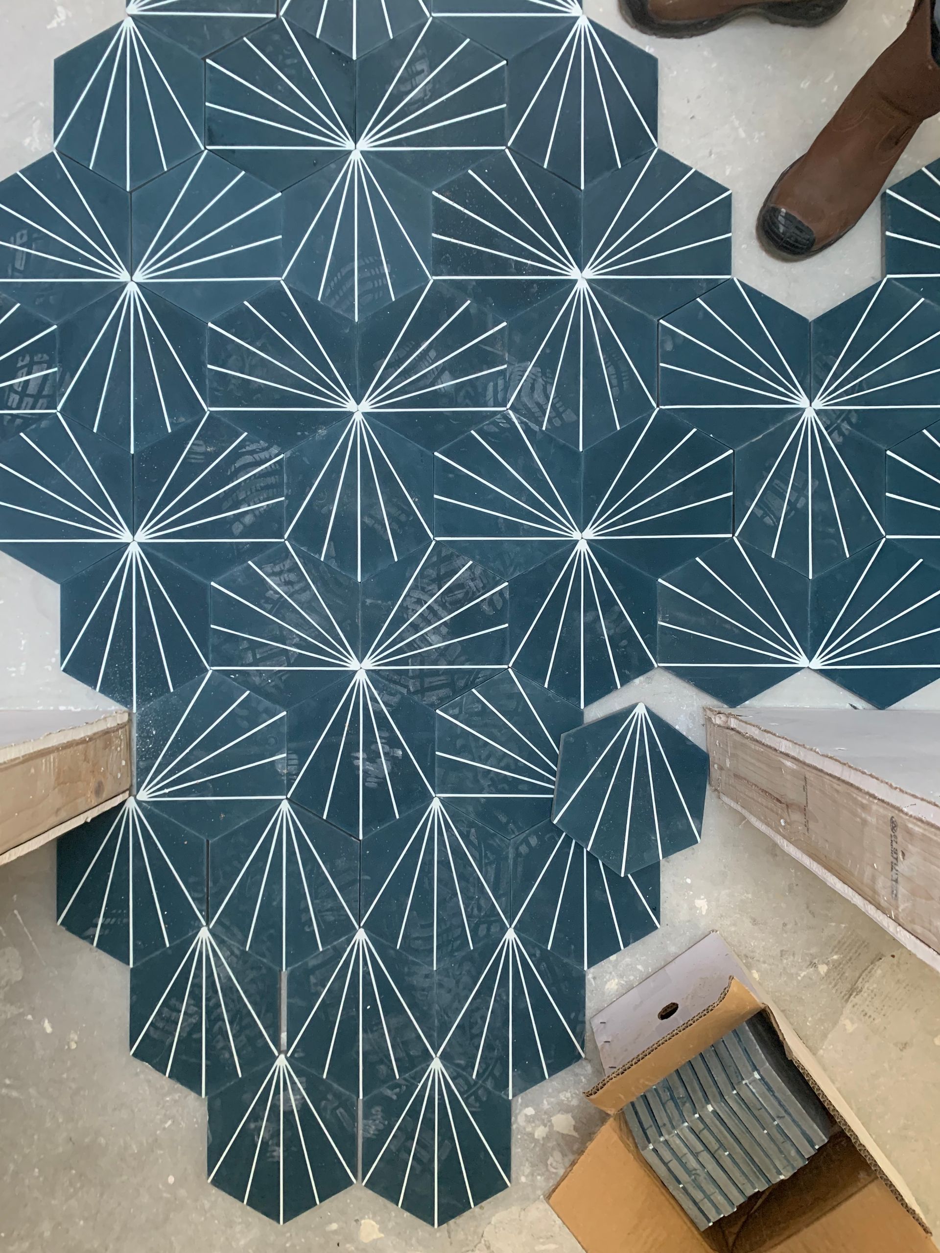 Blue geometric-patterned rug on a tiled floor, with a person’s shoes and a staircase visible nearby