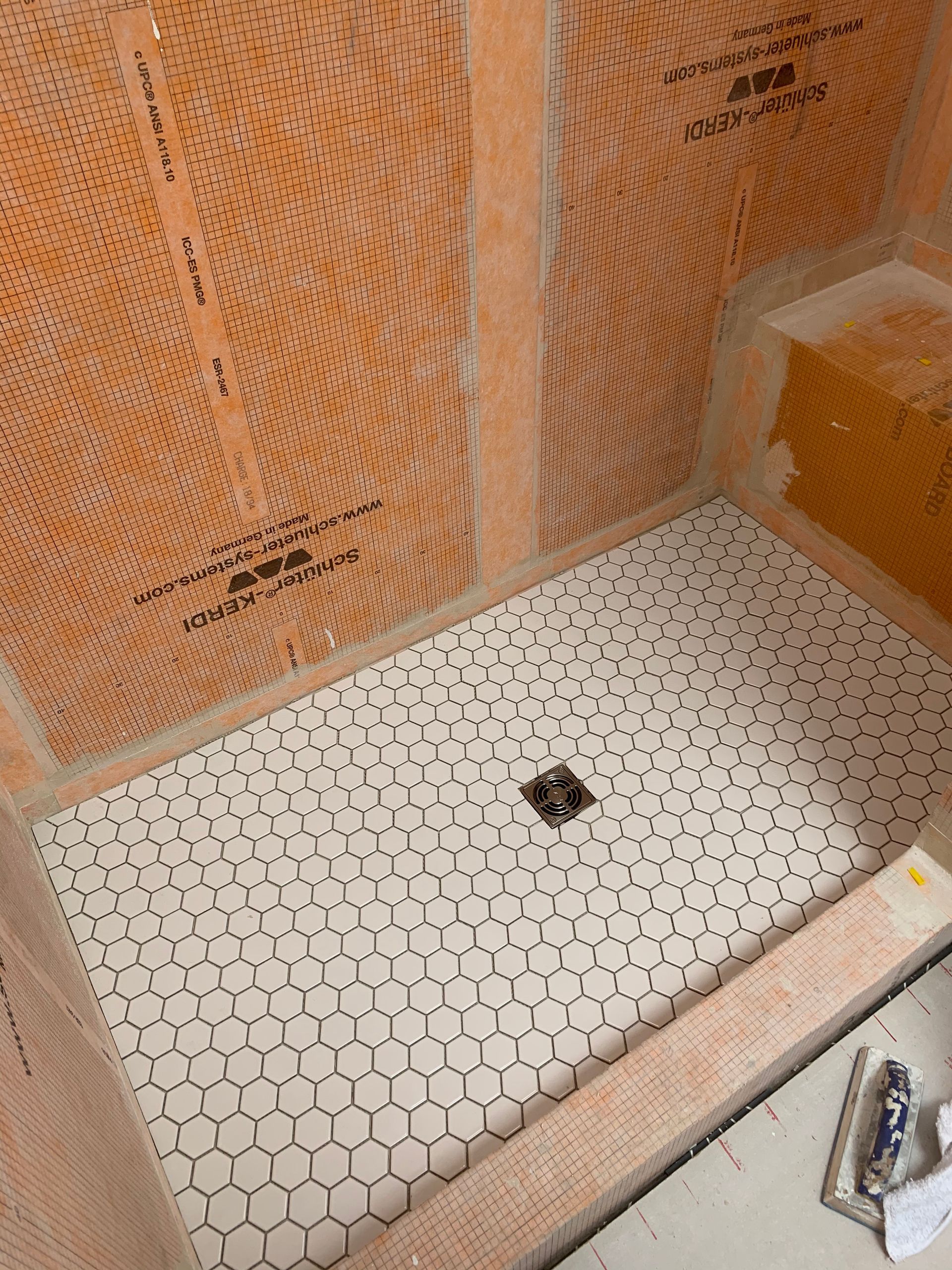 Small tiled shower floor with a central drain and orange waterproofing walls under construction