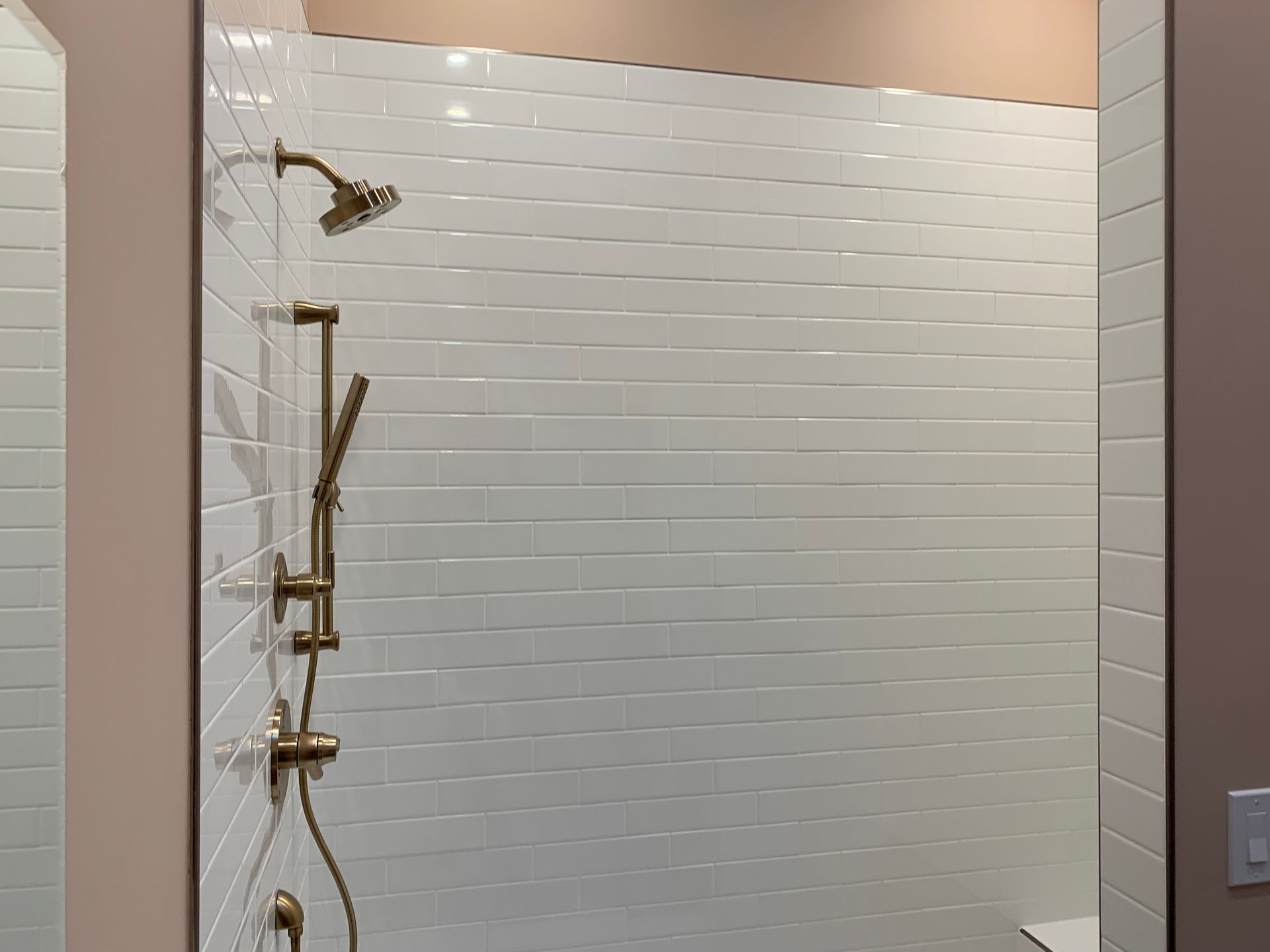 Empty shower stall with white tile walls and gold shower fixtures