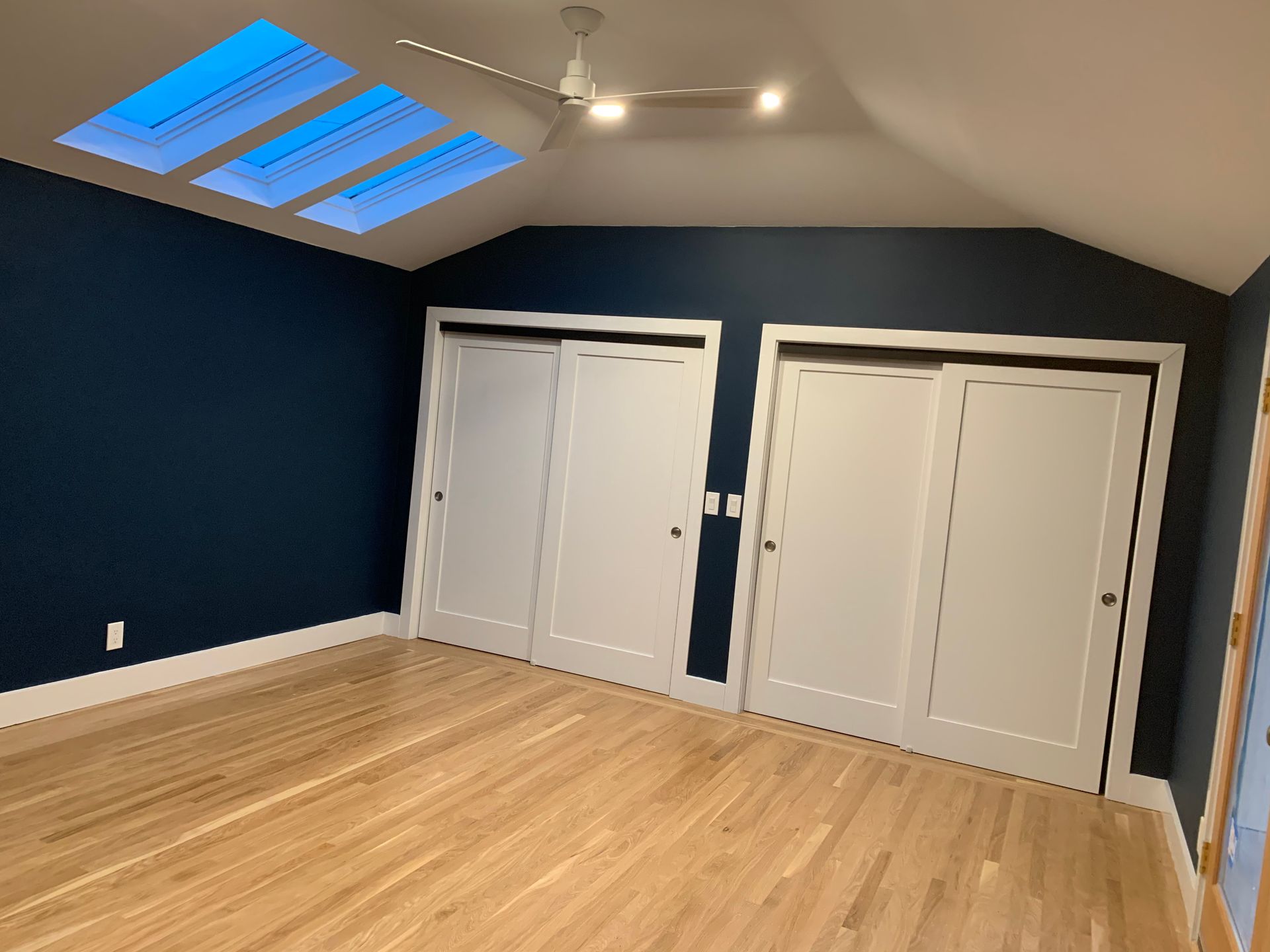 Empty attic-style room with dark blue walls, light wood floor, skylight, and double closet doors.