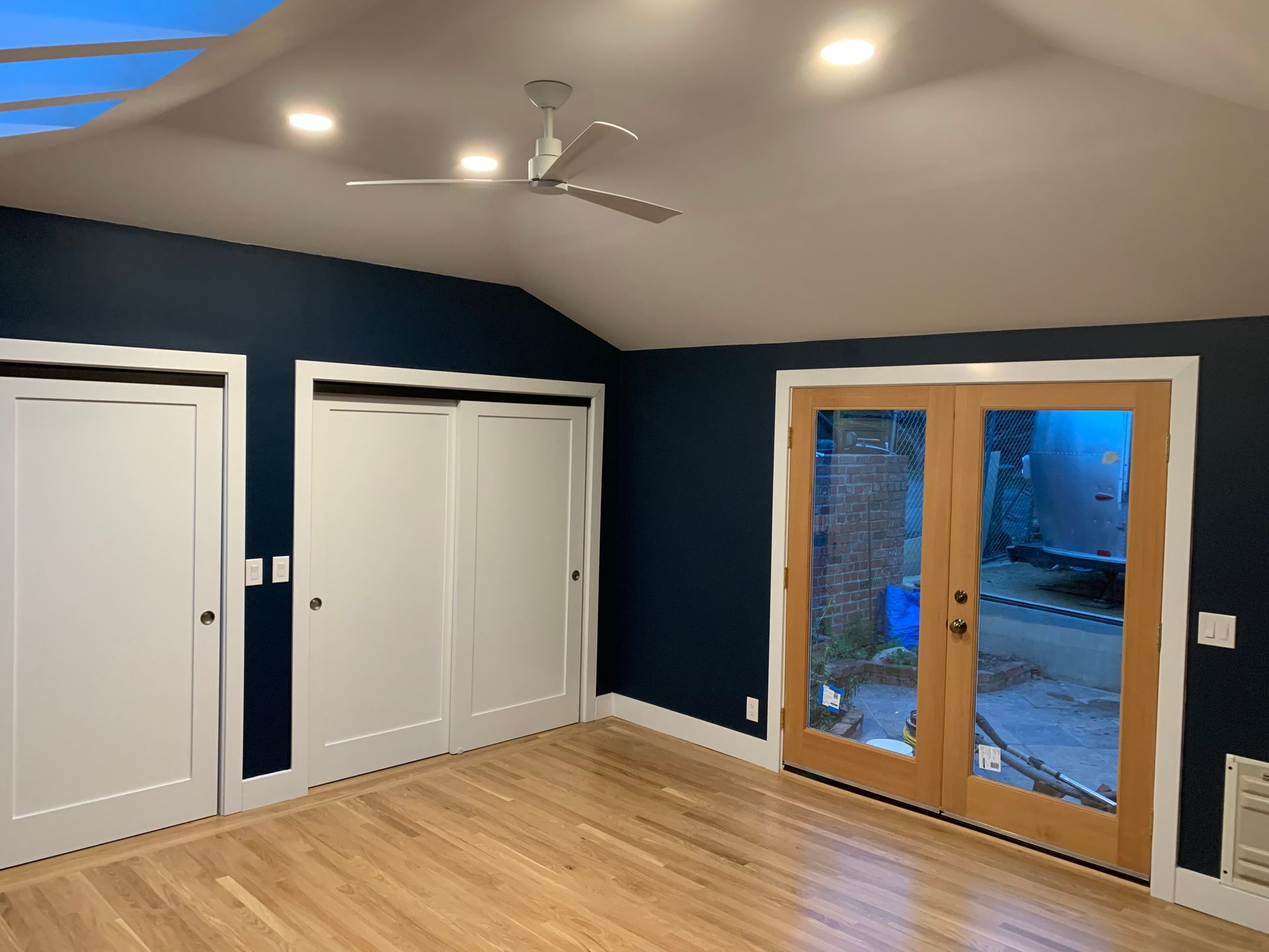Empty bedroom with dark blue walls, white closets, wood floor, and glass doors to a patio.