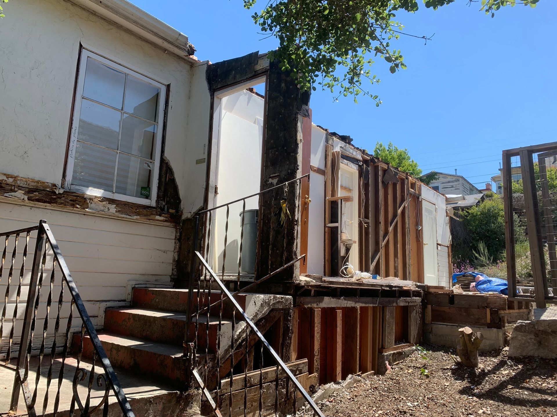 Exterior of a damaged house with a collapsed porch, broken stairs, and exposed wooden framing