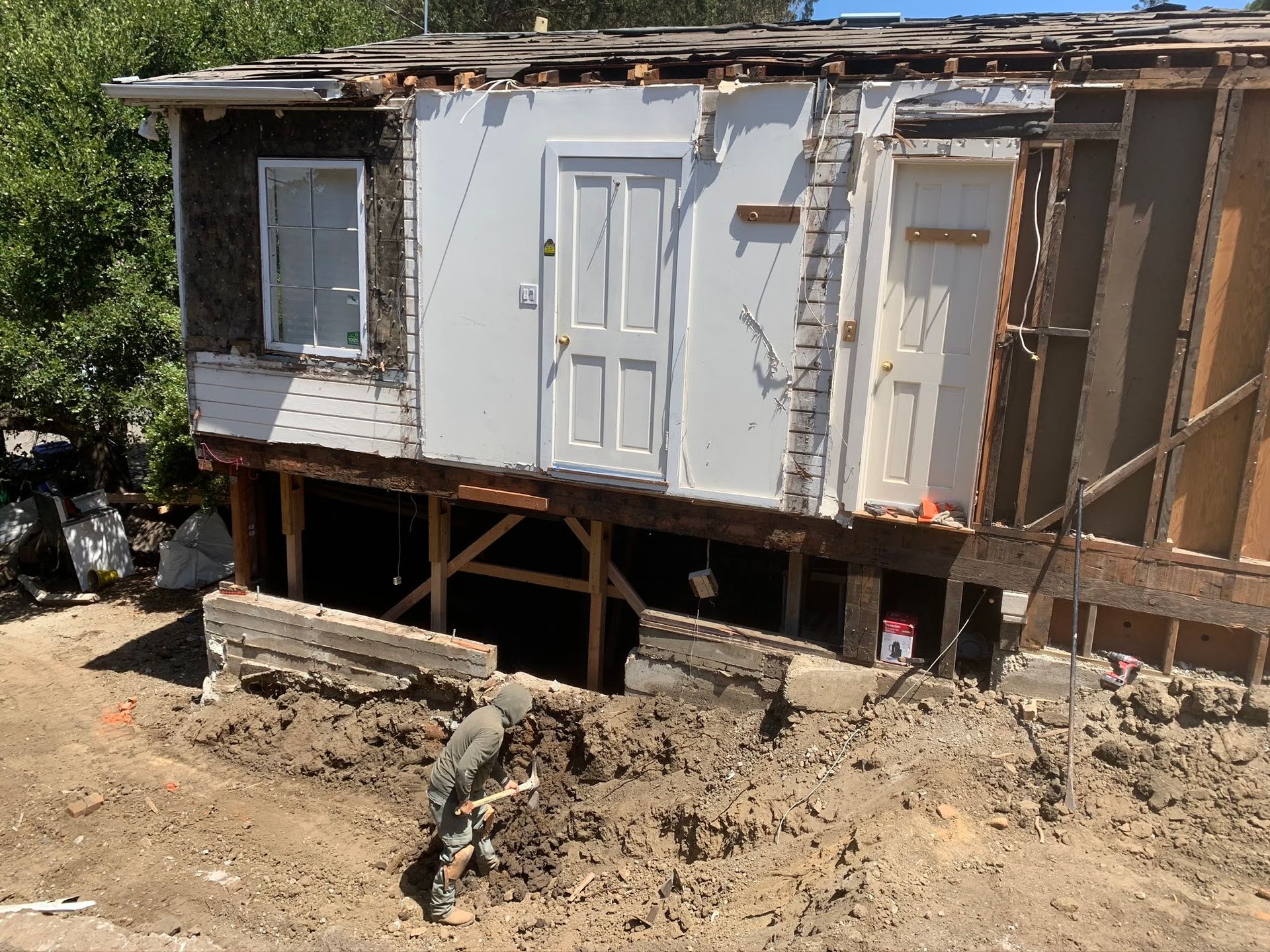 Partially demolished white house with exposed framing and rubble in the dirt yard