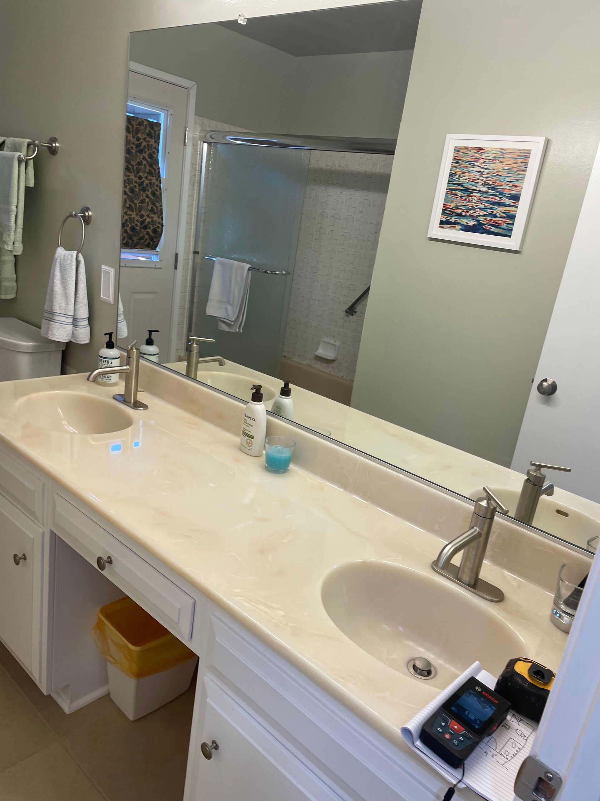 Bathroom vanity with double sinks, large mirror, shower in background, and toiletries on the counter