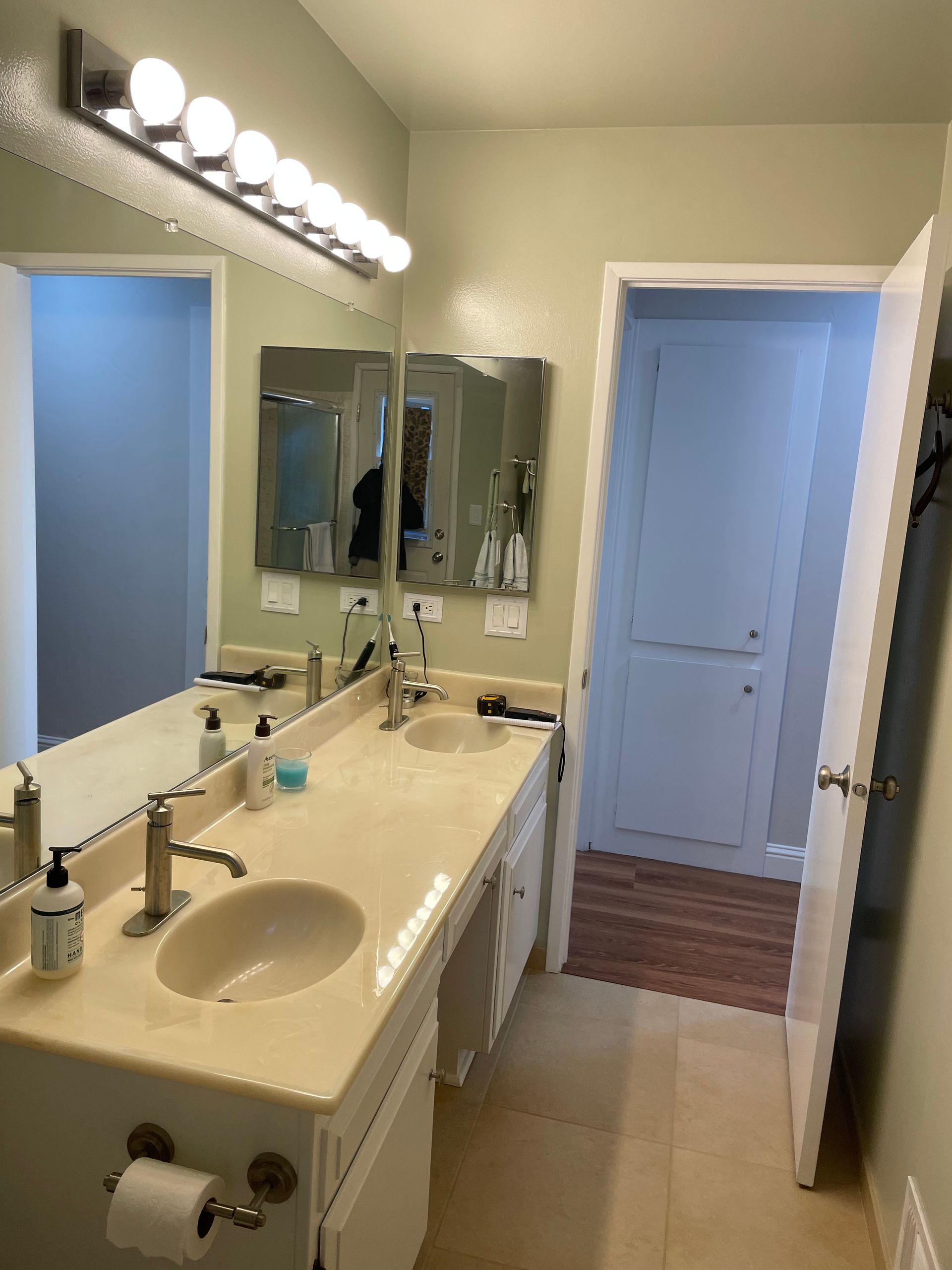 Bright bathroom vanity with double sinks, large mirror, and overhead lights beside a shower door